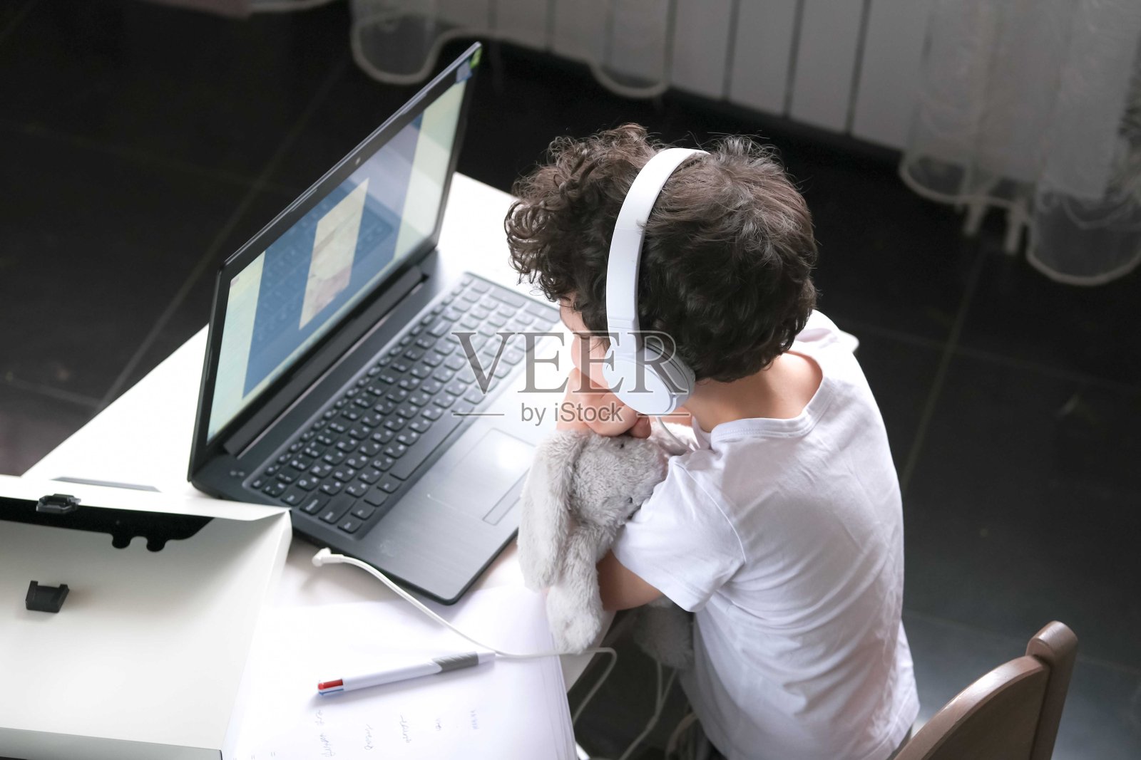 男孩戴着耳机在电脑前。照片摄影图片