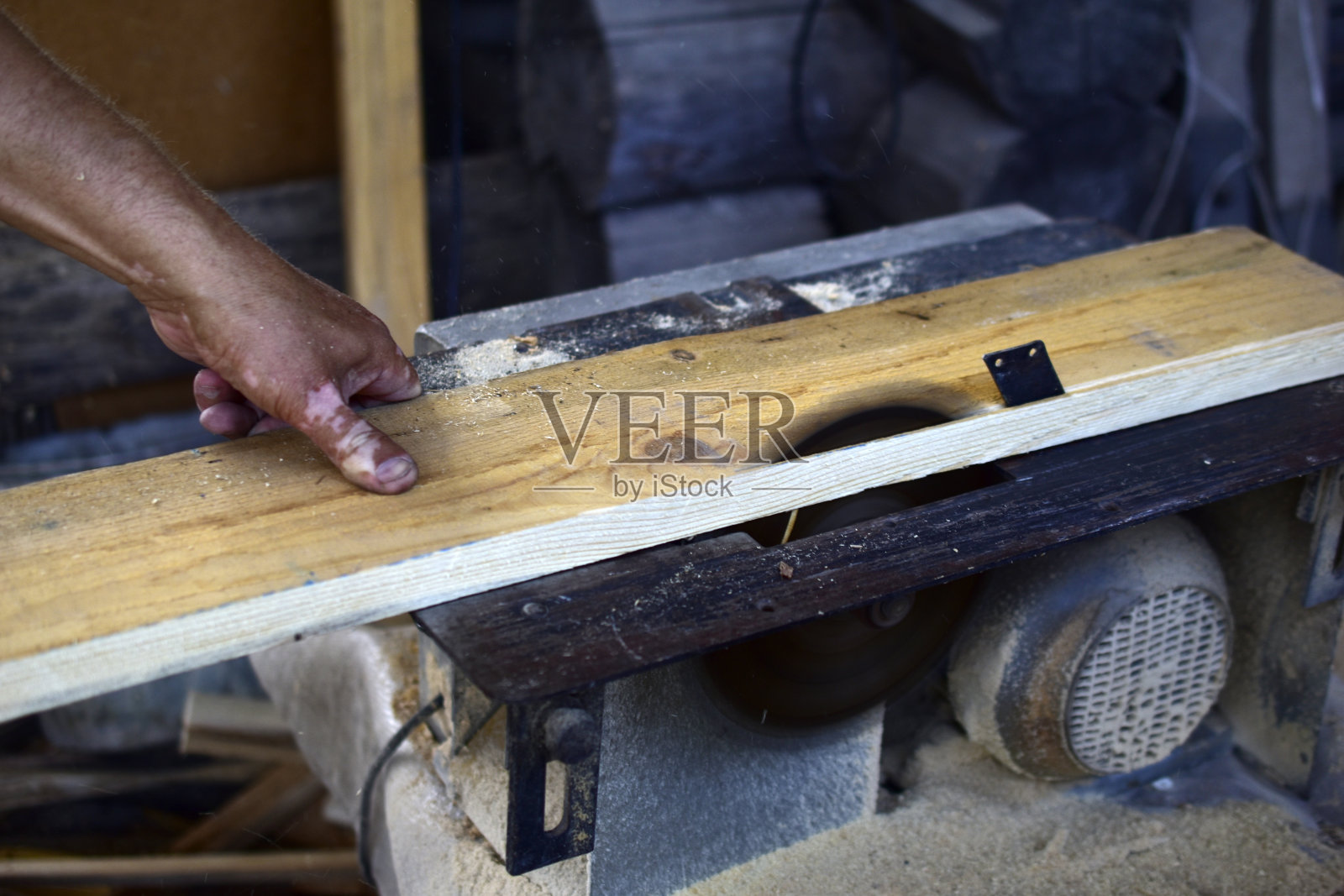 一个人在圆形锯木厂切木板。用圆锯工作的一个人的皮肤有色素沉着的手照片摄影图片
