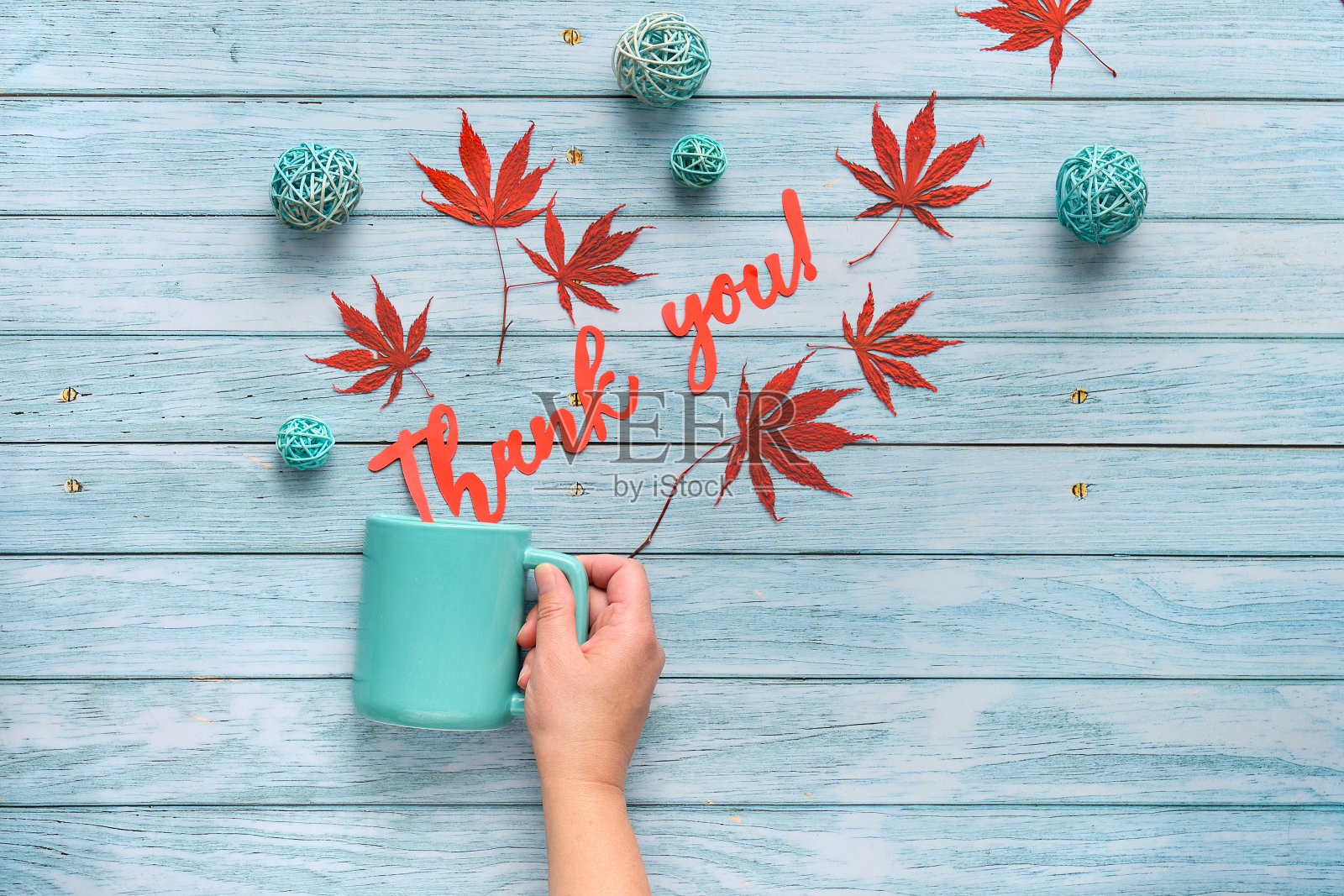 秋平铺在浅灰色的陈年木材、枫叶和藤球上的秋装饰。手持陶瓷杯，上面写着“谢谢你”。照片摄影图片