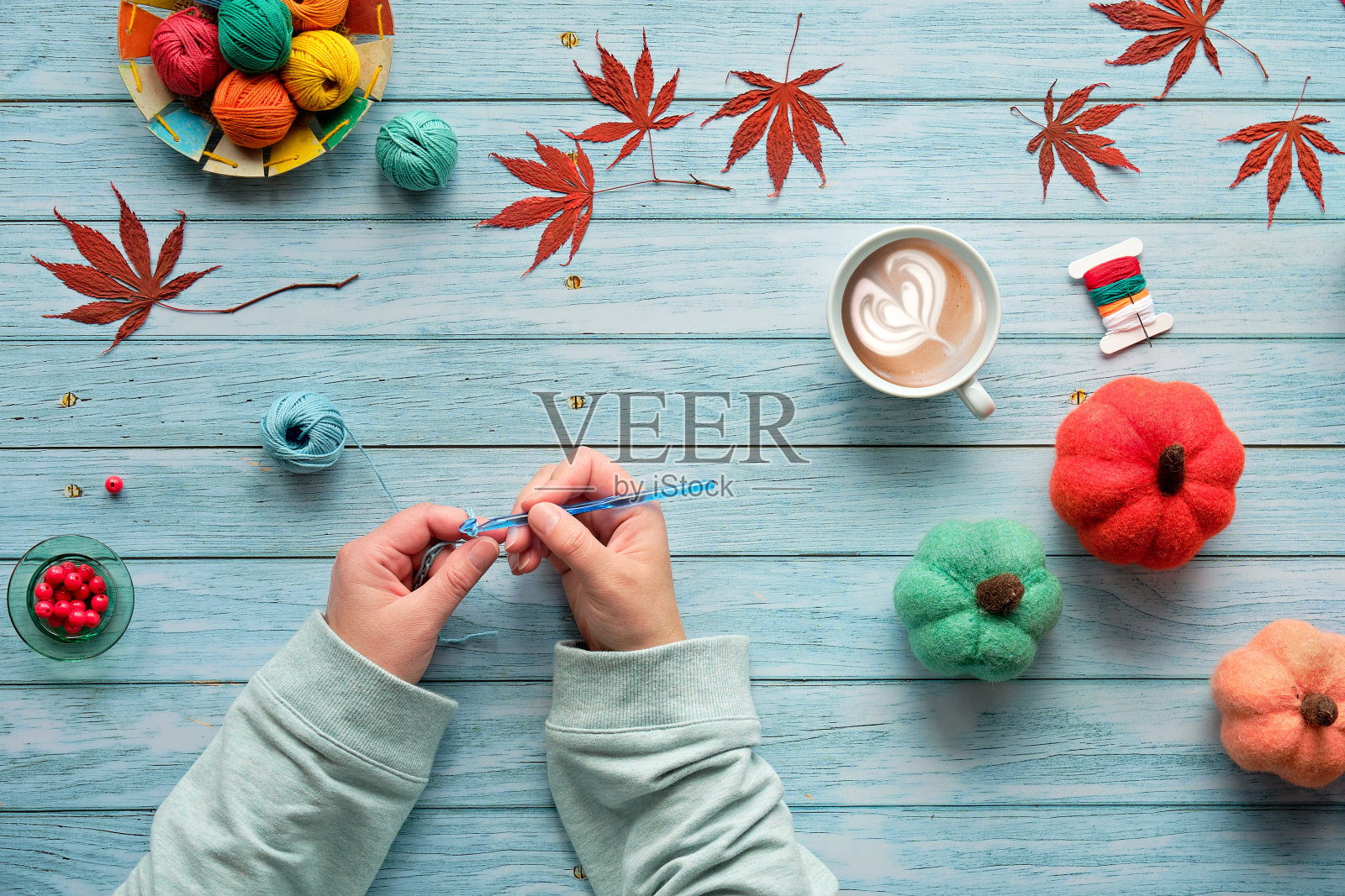 女人用手编织钩针。俯视图的木制桌子与纱线球，羊毛束，装饰的秋天感觉南瓜和秋天的叶子。季节性的平铺在淡蓝色褪色的木头上。照片摄影图片