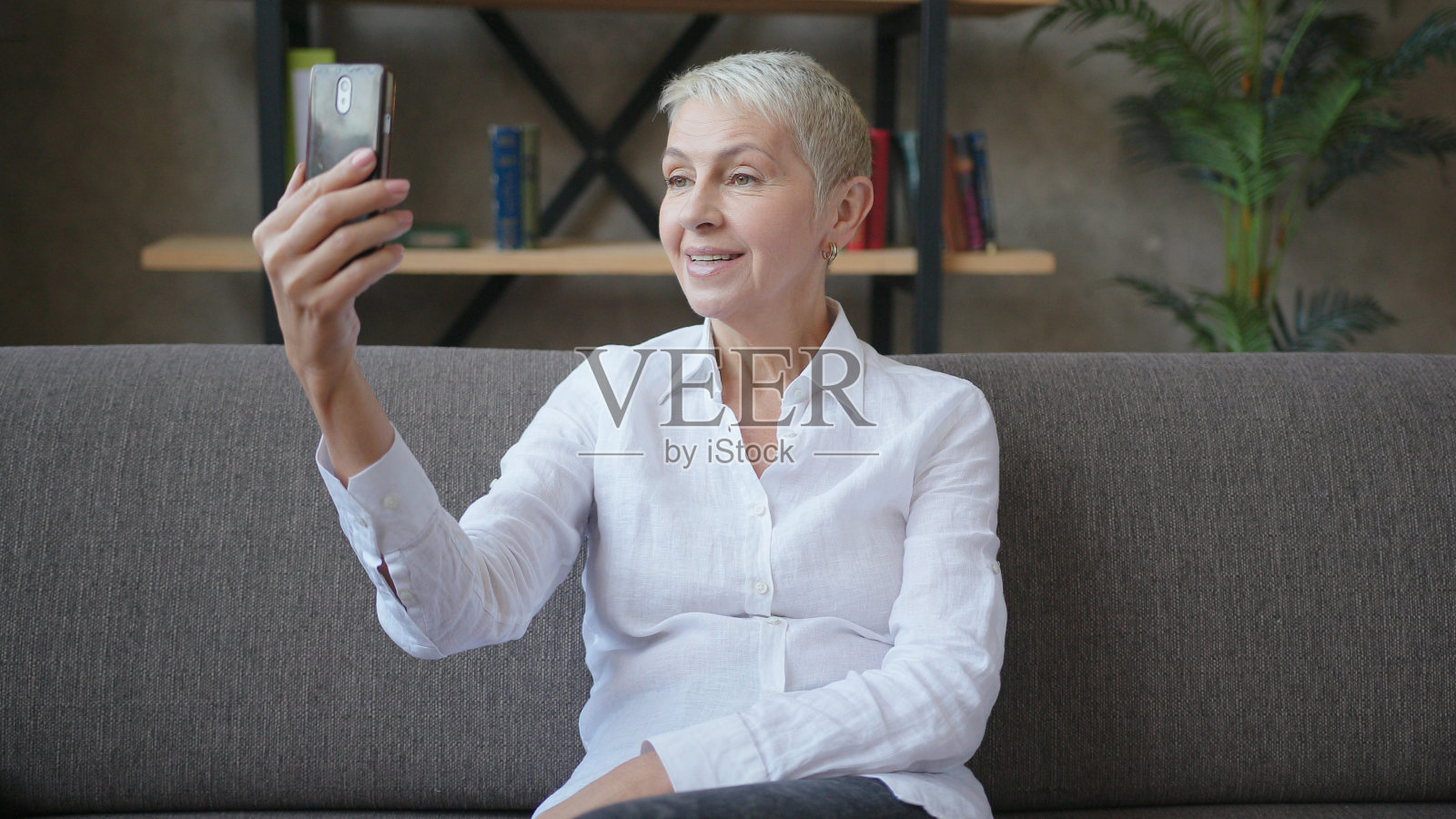 上了年纪的成功商业女性坐在沙发上用智能手机进行视频通话照片摄影图片