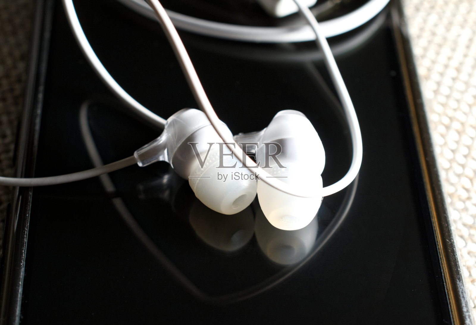 黑色智能手机屏幕上的白色耳机，静物。照片摄影图片