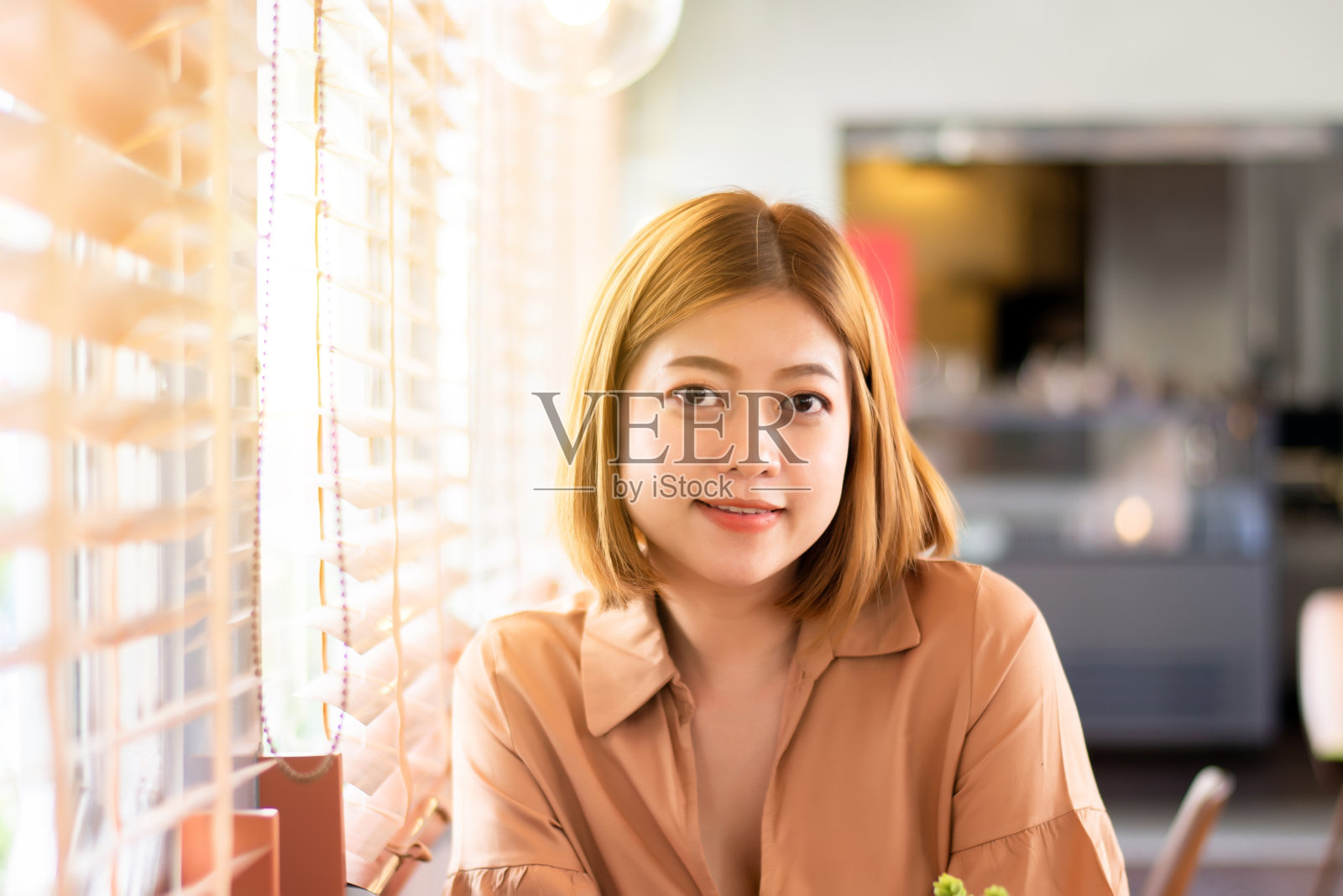 快乐的年轻亚洲女人坐在和看着相机在咖啡馆，微笑的脸照片摄影图片