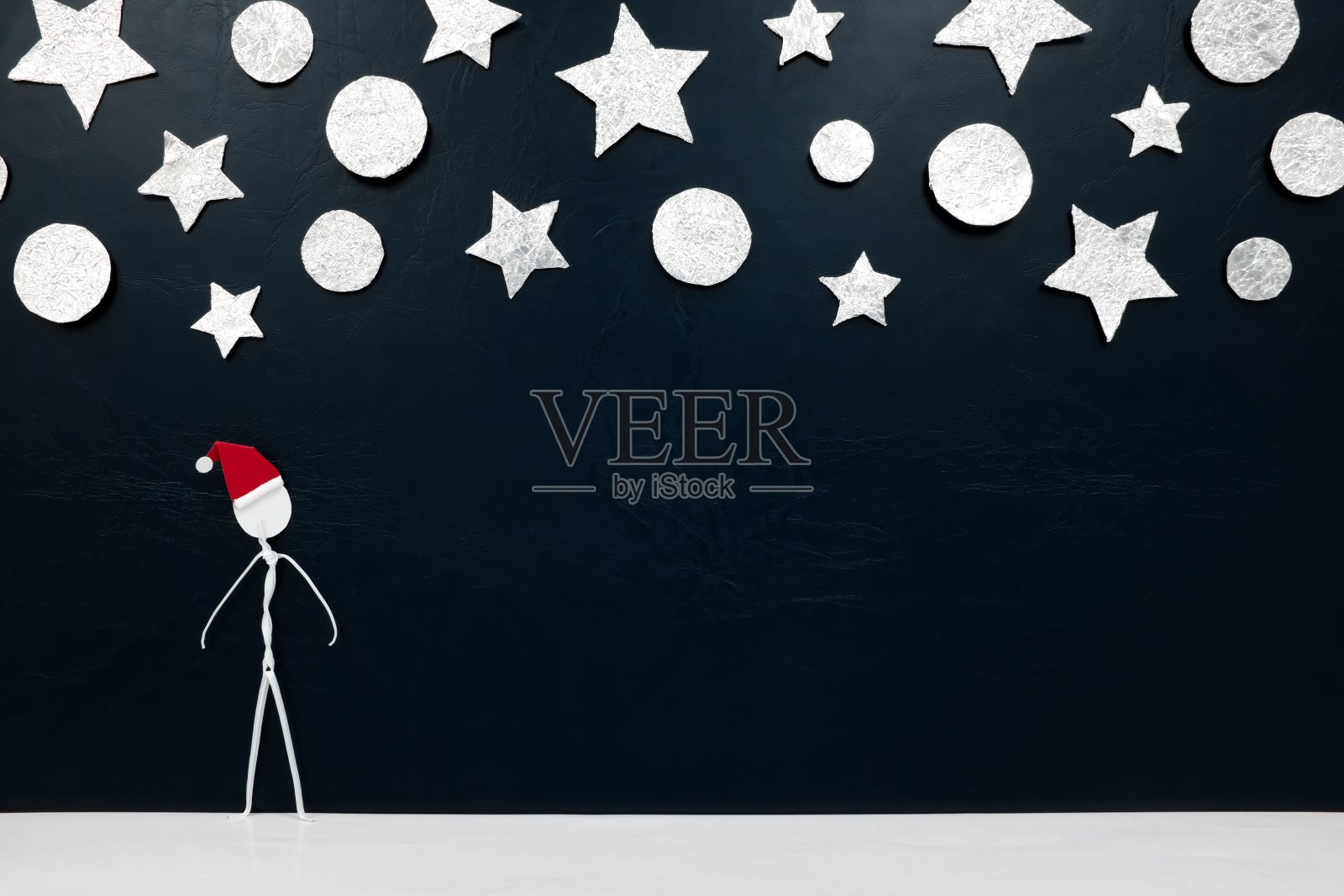 一个单独的棍棒人在圣诞帽单独在一个黑色背景与银色圣诞装饰。照片摄影图片