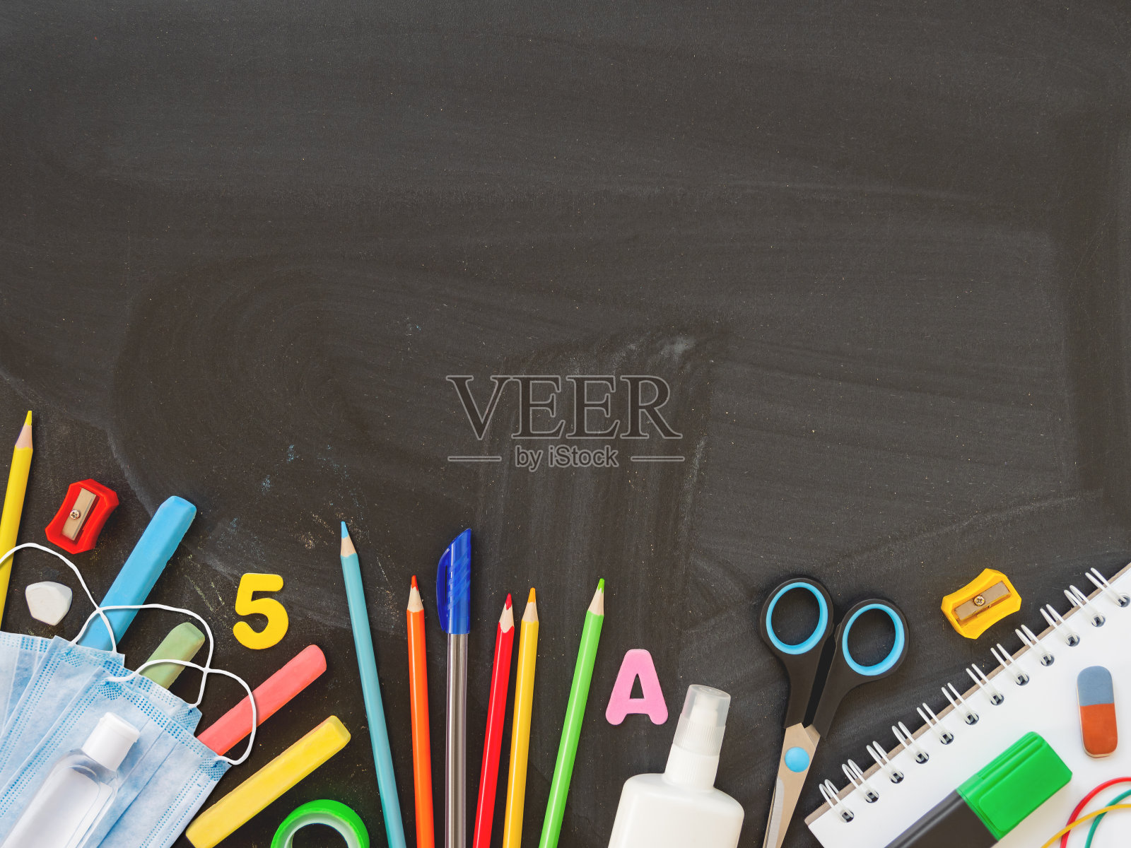 俯视图上的彩色文具，防护医疗口罩和洗手液。回到学校平铺的概念。水平黑板背景与复制空间。学校购物。新常态照片摄影图片