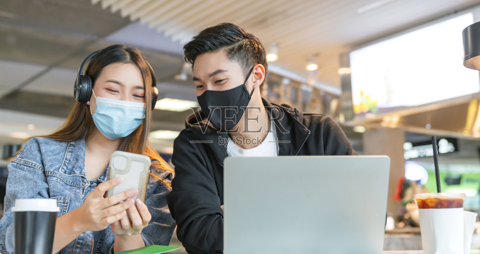 快乐的亚洲夫妇戴着防毒面具在咖啡店享受良好的交谈。年轻的男子和女子在一家餐馆看着触摸屏电脑一起笑照片摄影图片