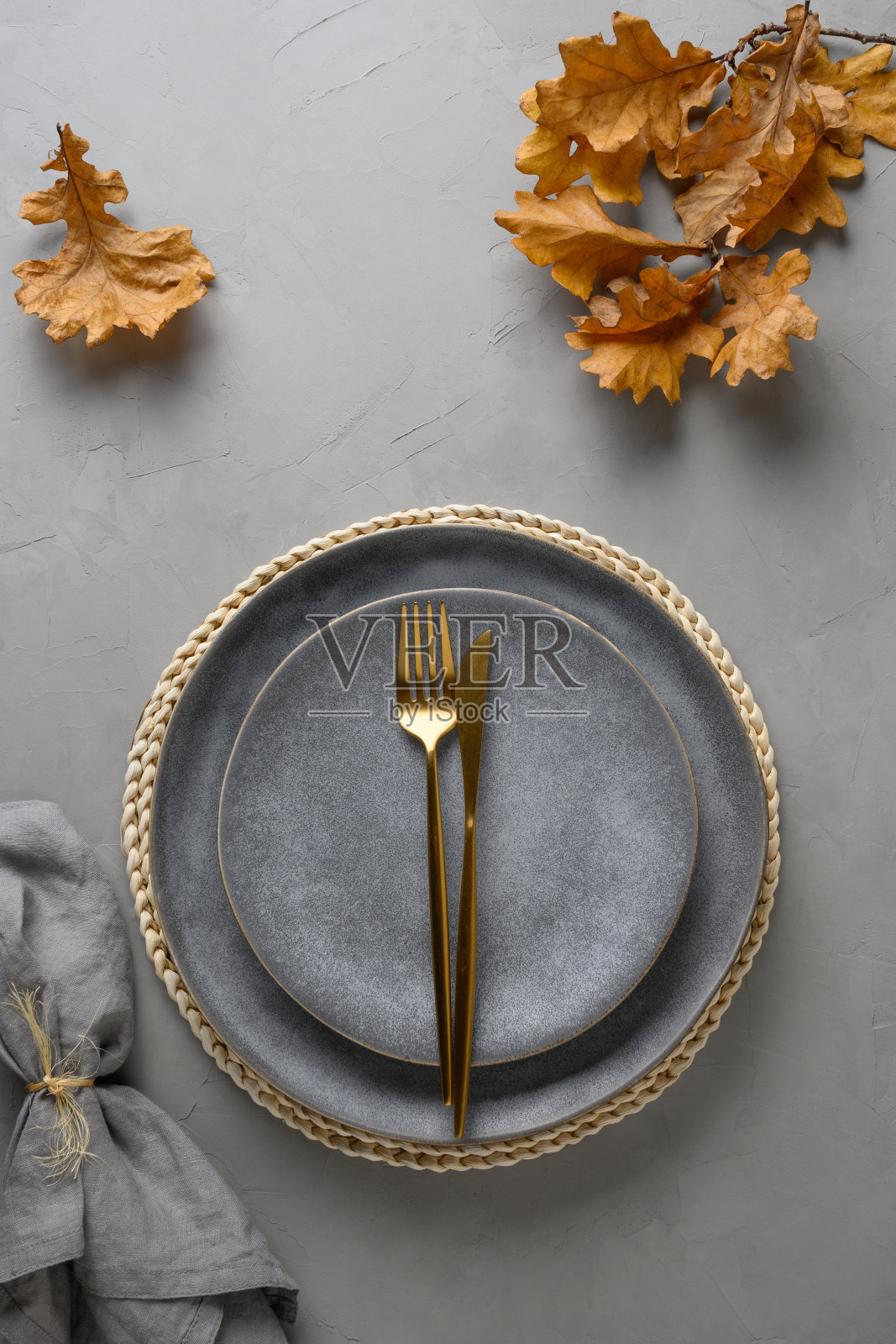 优雅的餐桌设置与秋天的橡木叶和金色的餐具在灰色的背景。平躺，俯视图照片摄影图片
