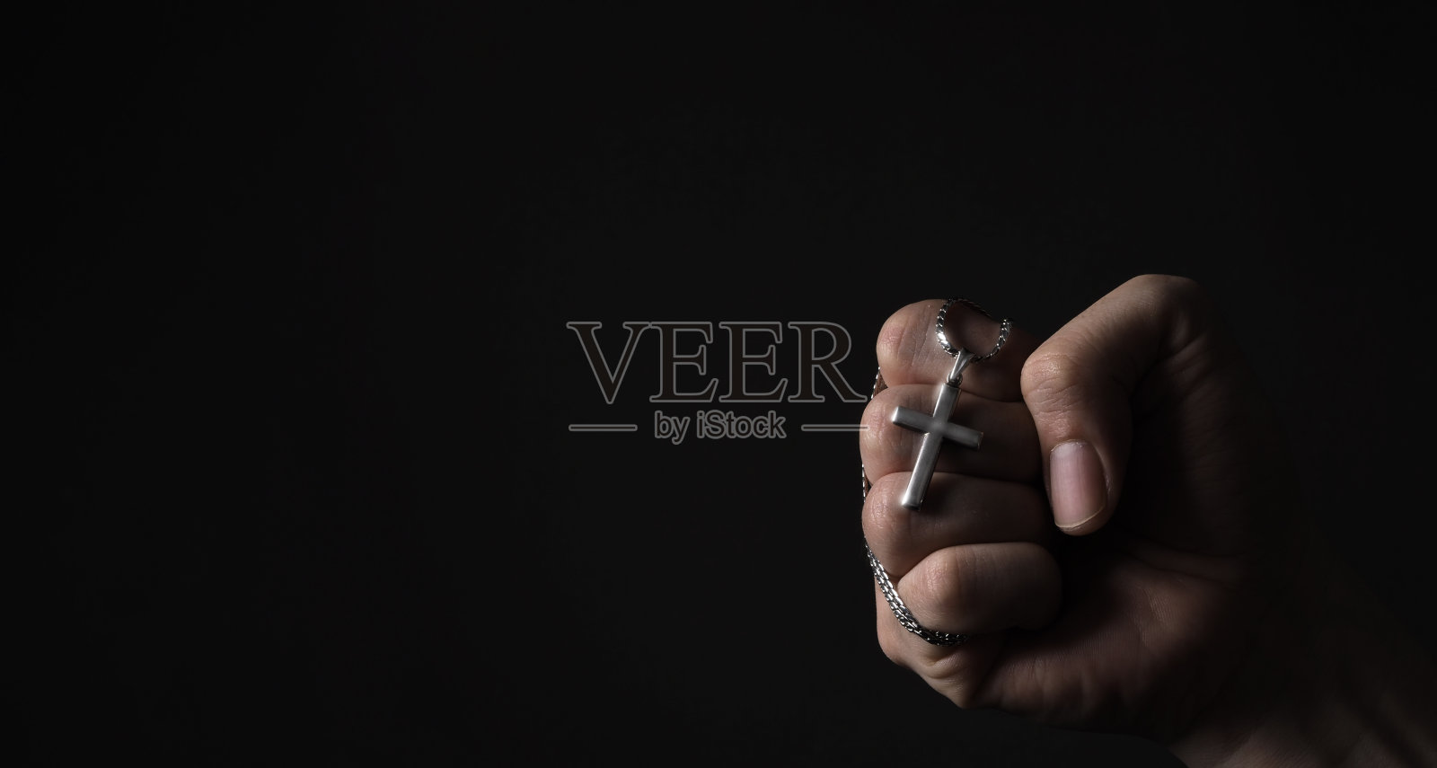 十字架吊坠或十字符号，由银制成，并在人的手中。代表为世界大流行冠状病毒死亡的人祈祷，特写黑色背景照片摄影图片