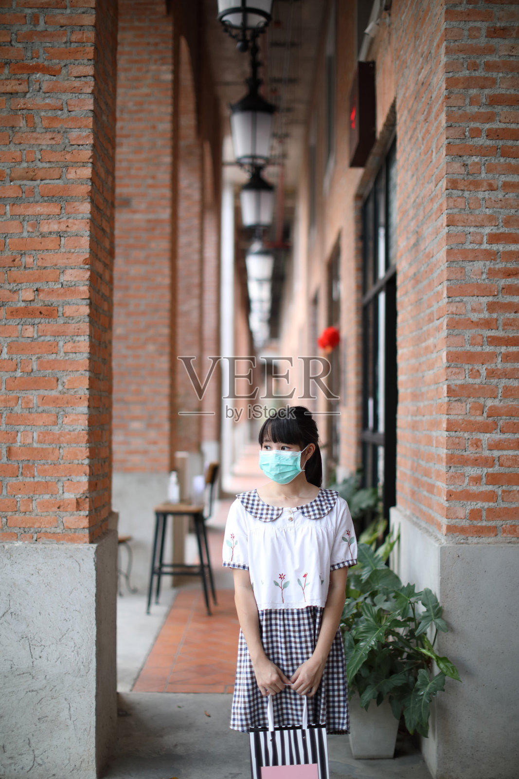 描绘新冠肺炎疫情暴发时，一名年轻女性戴着口罩在城市社区购物中心购物照片摄影图片