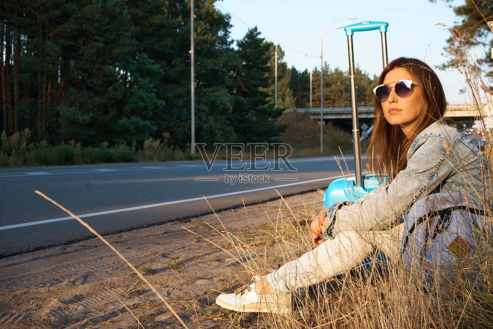 一个女孩带着一个手提箱搭便车。森林里的路。搭便车照片摄影图片