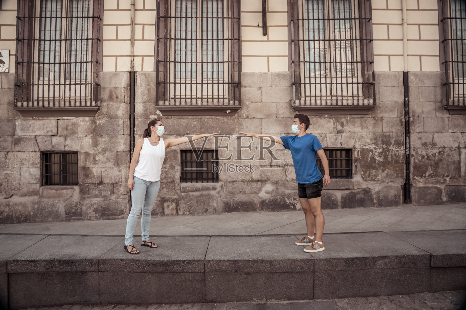 一男一女戴着防护口罩，彼此站着2米远，保持社交距离，避免新冠病毒的传播。新冠肺炎疫情防控与新常态的概念形象。照片摄影图片