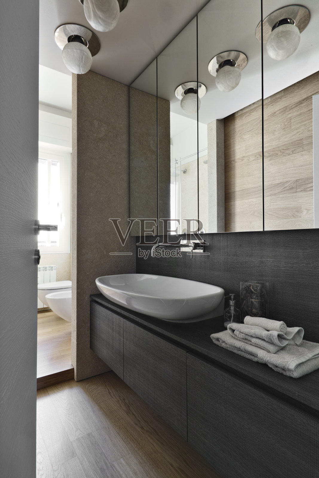 室内拍摄的现代浴室的前景，柜台顶部的洗脸盆在木制家具上，地板是木制的照片摄影图片