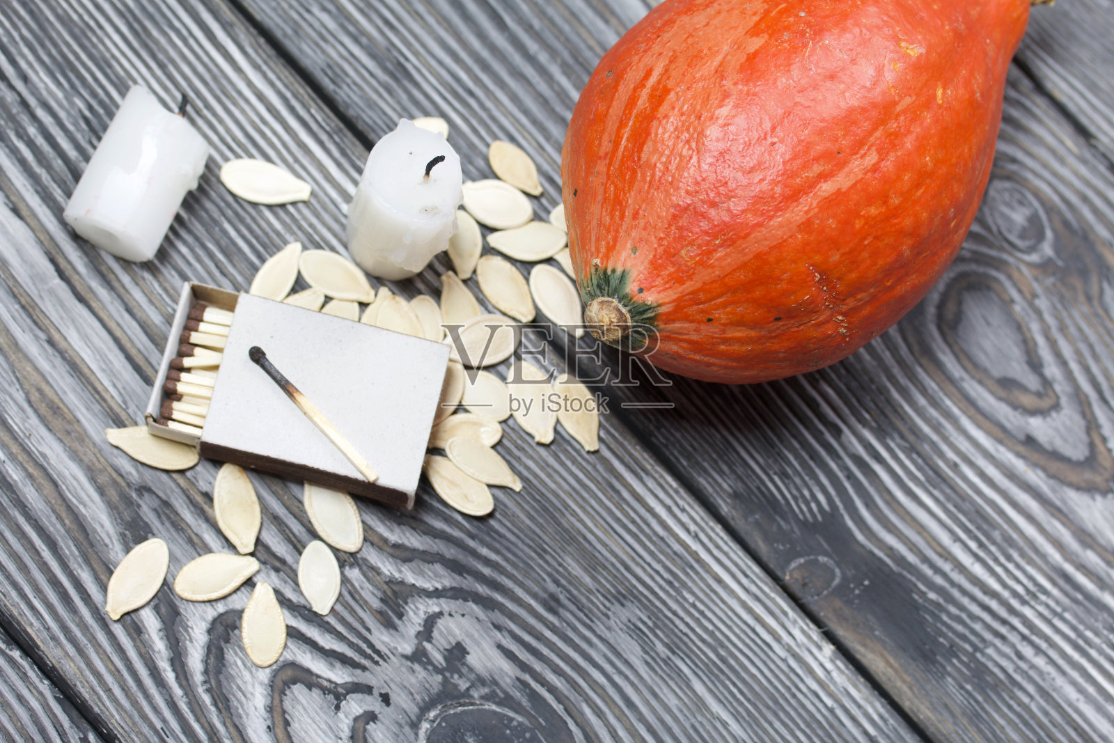 橙色南瓜，种子和蜡烛头。在一盒火柴旁边。在刷成黑色和白色的松木板上。照片摄影图片