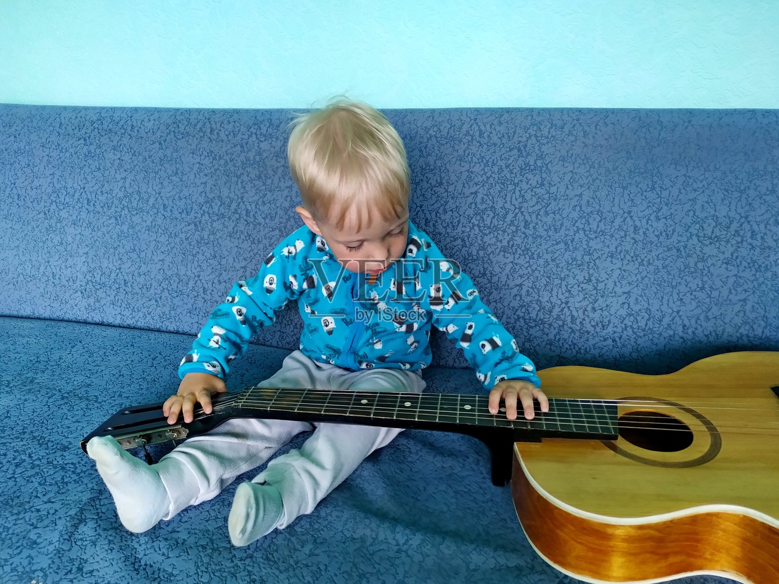 蓝色沙发上的小男孩饶有兴趣地看着一把复古吉他照片摄影图片