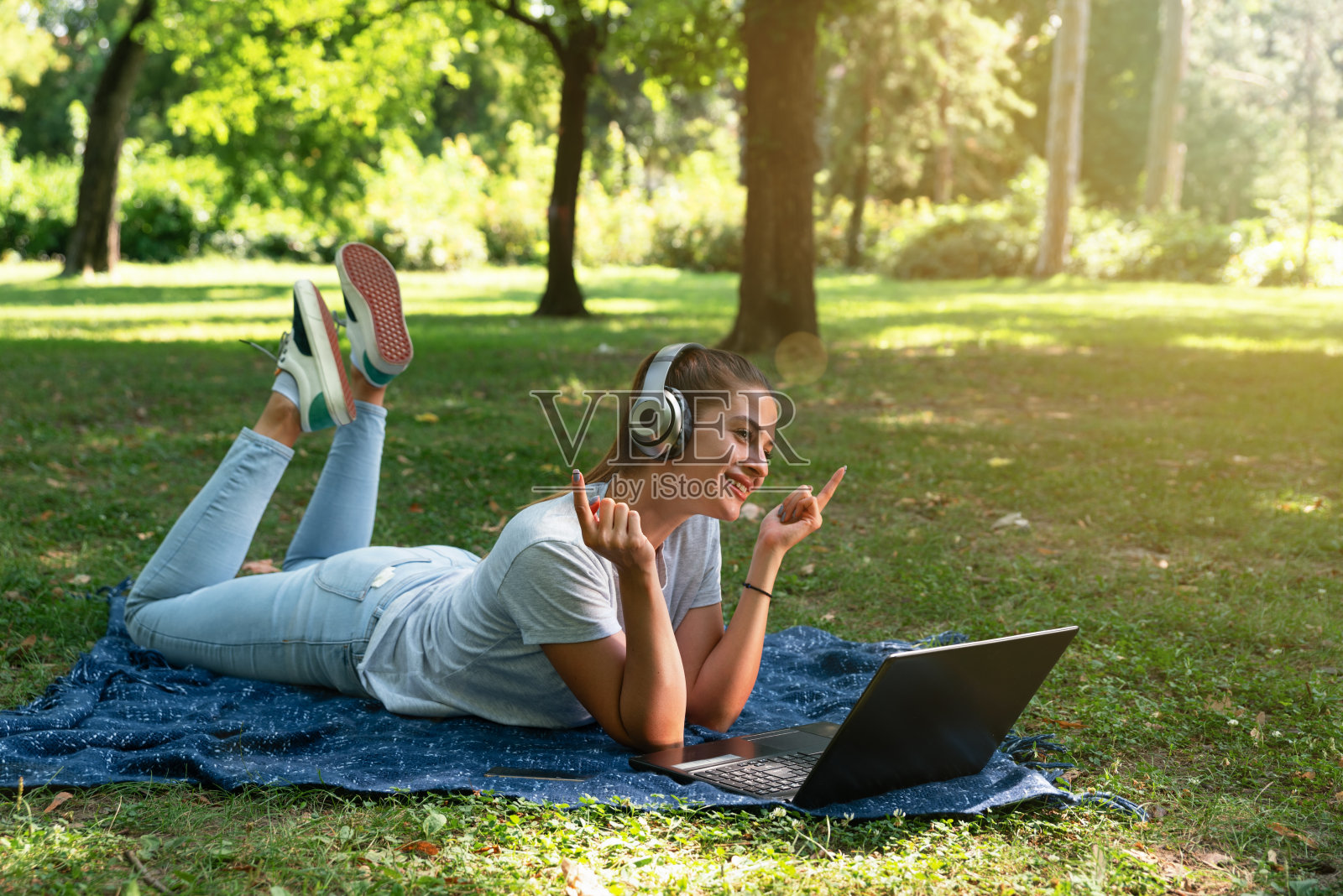 年轻漂亮的女孩躺在公园里，头上戴着无线耳机听着音乐，玩得很开心照片摄影图片