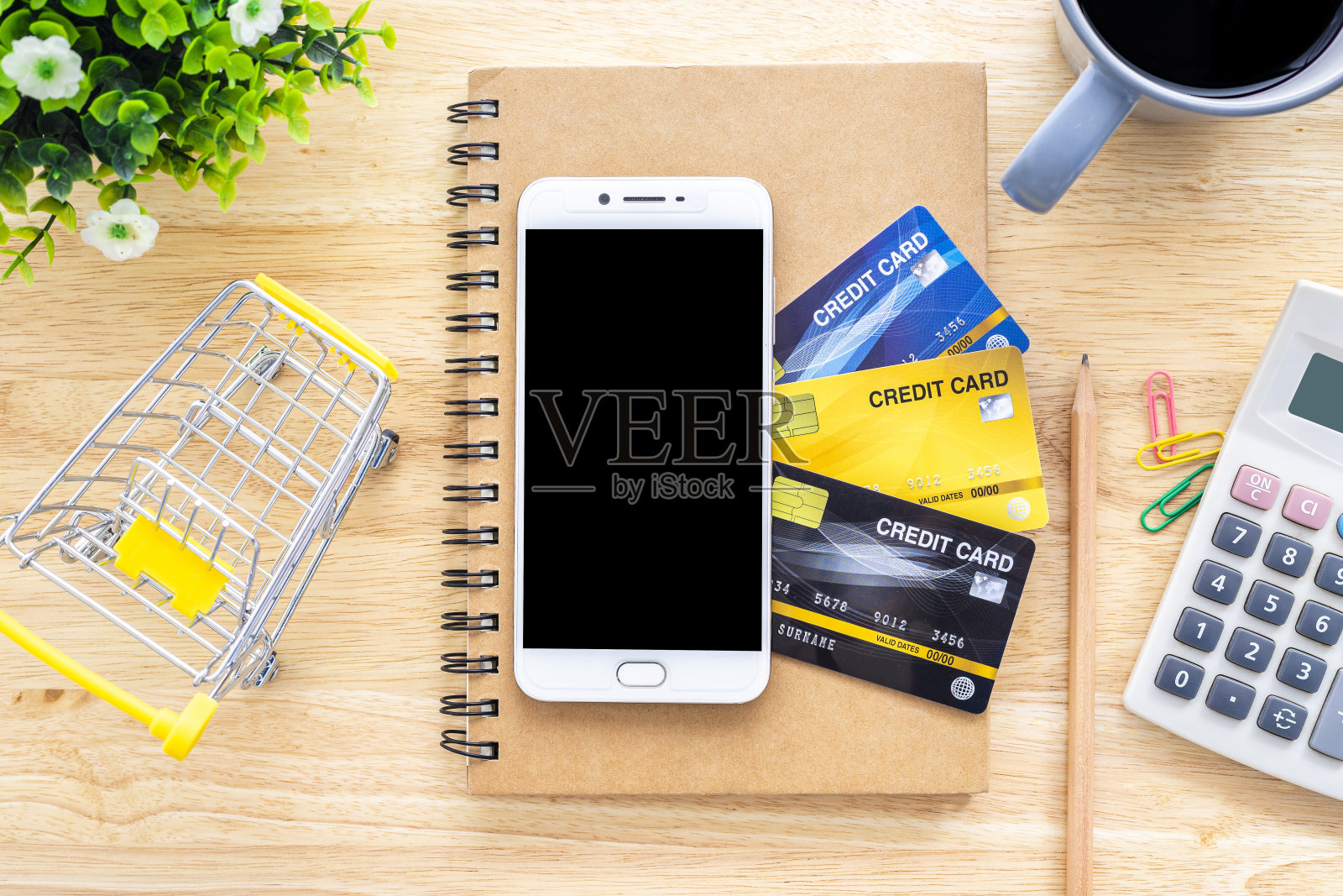 智能手机上的信用卡，笔记本，花盆树，购物车，计算器和咖啡杯木制背景，网上银行概念，顶视图办公室桌子照片摄影图片