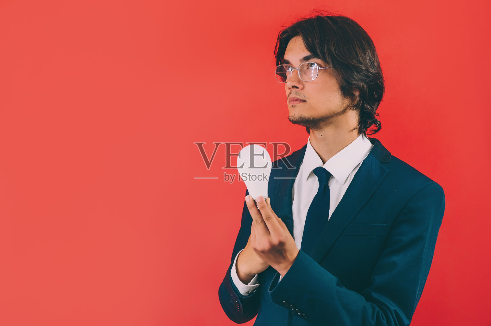 一个商人，手里拿着一个灯泡，背景是红色的。概念关于主题的思想。照片摄影图片