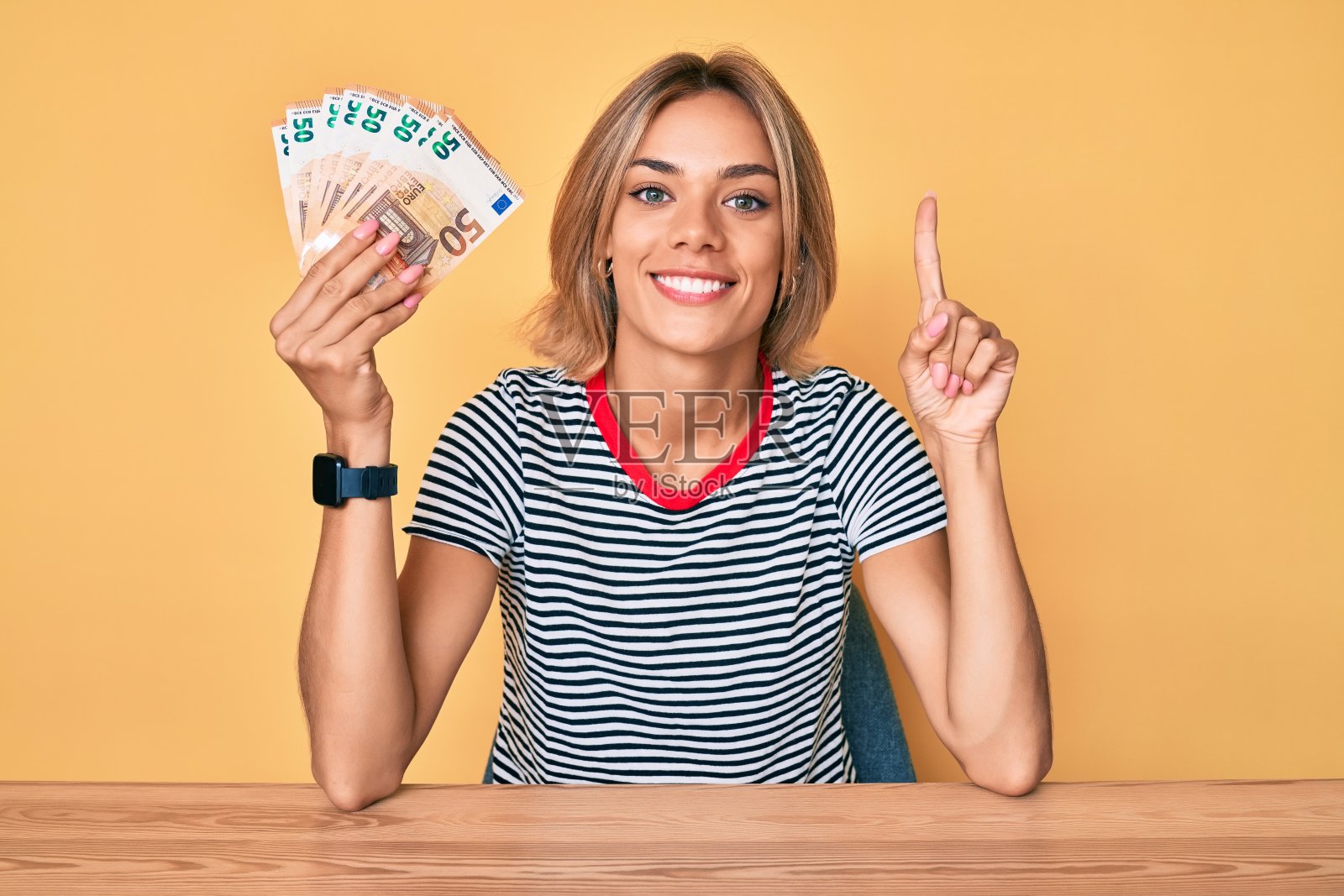 漂亮的白人女人拿着50欧元钞票微笑着提出一个想法或问题，用手指着幸福的脸，第一照片摄影图片