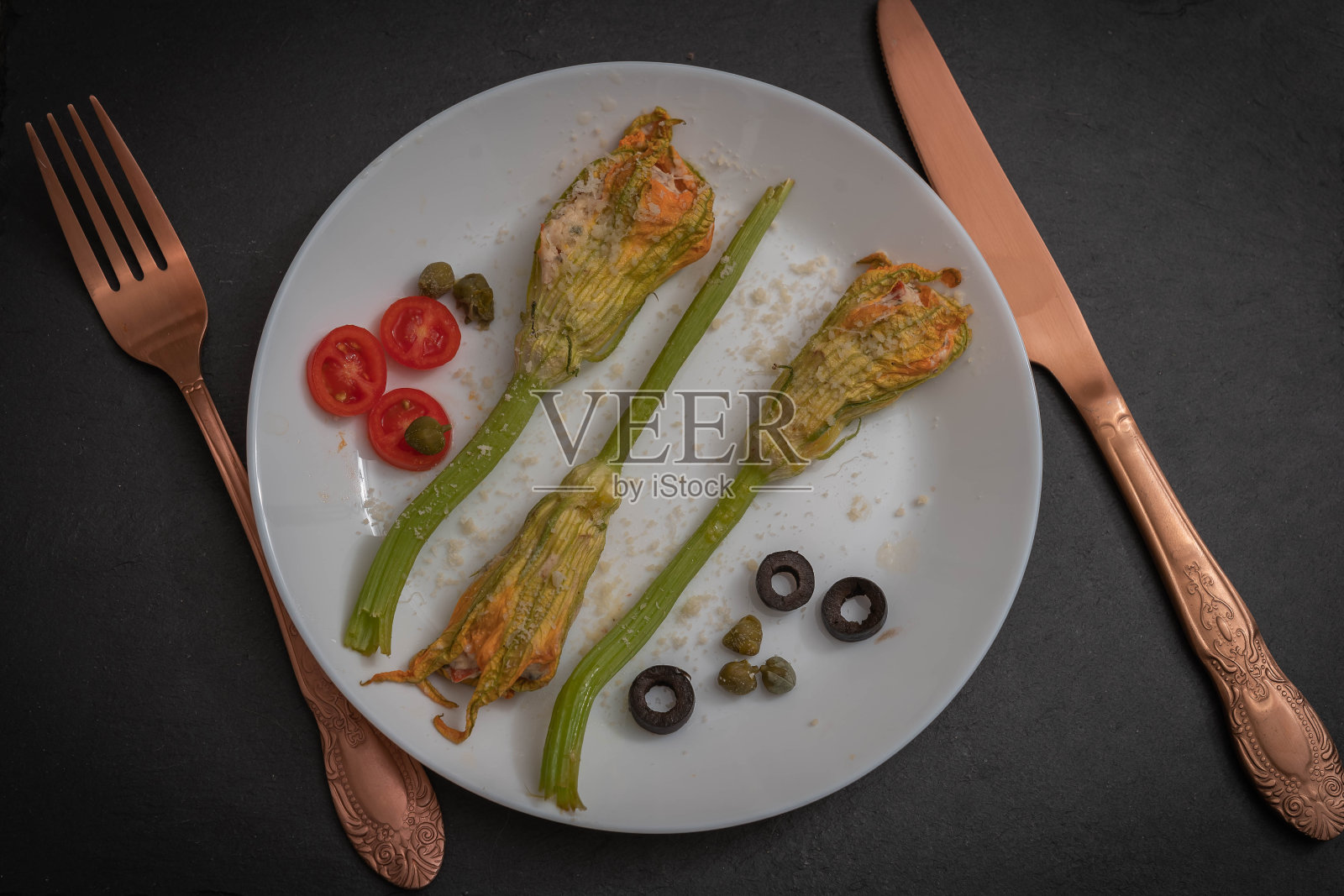 白色的盘子上放着填馅的西葫芦花，配上一把叉子和一把老式的小刀，背景是黑色的照片摄影图片