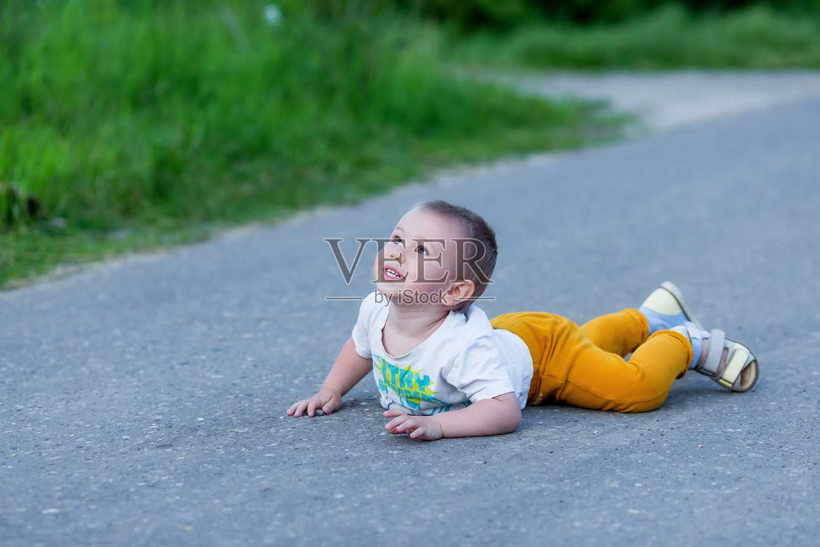 可爱的蹒跚学步的小男孩摔倒在公园路上照片摄影图片