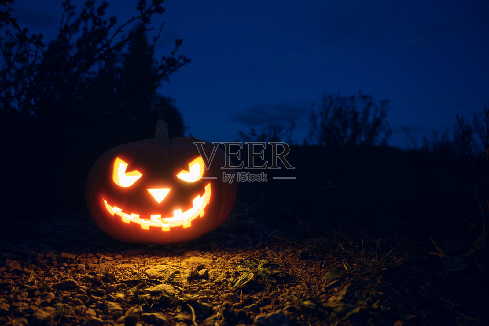 阴森可怖的万圣节南瓜晚上在地上发光。照片摄影图片