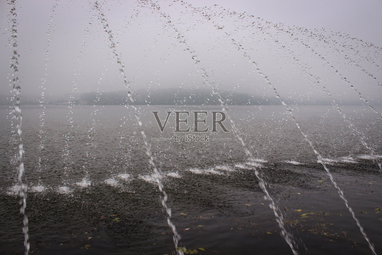 喷泉的喷流落入湖中，溅起许多水花。对岸在背景中几乎看不见，因为湖被雾覆盖着。照片摄影图片