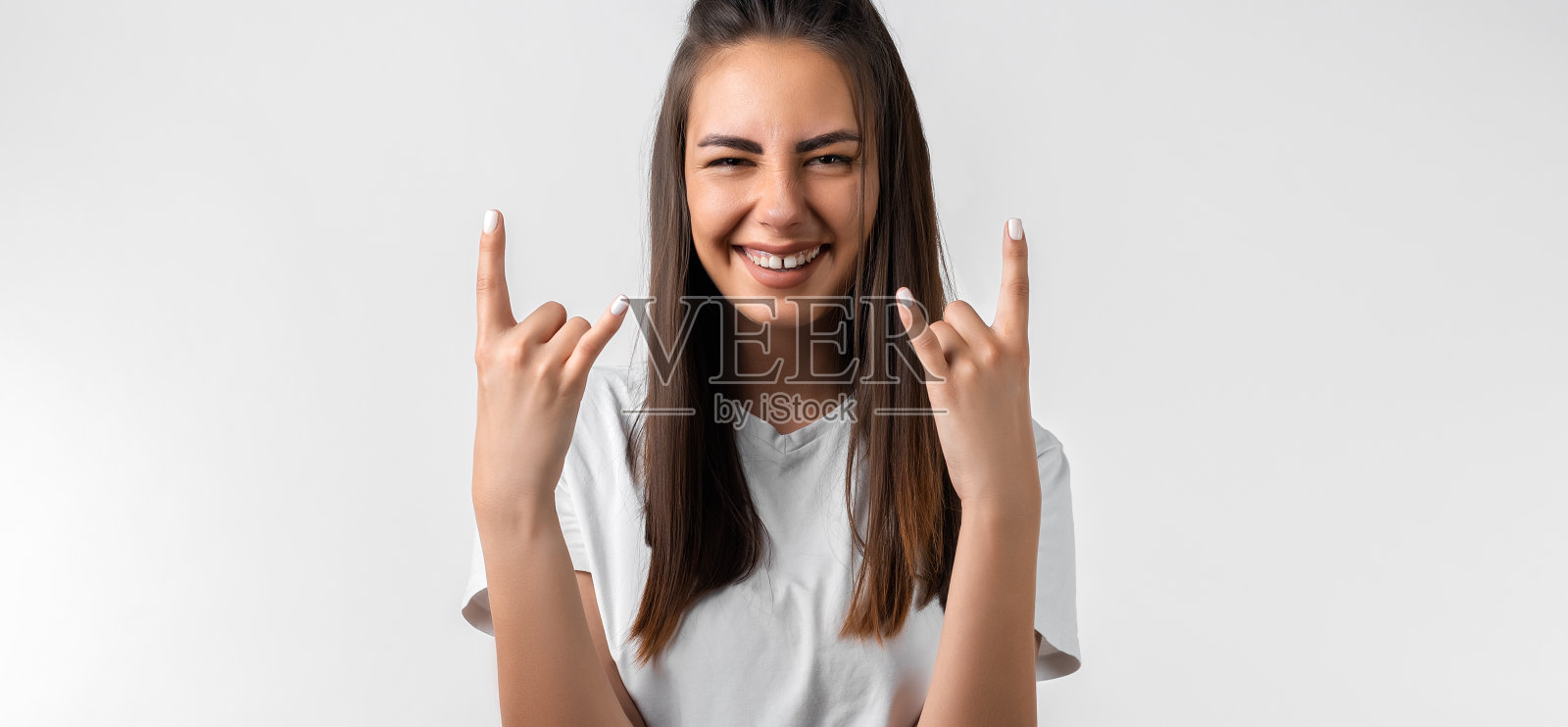 情绪化的女人，留着栗色的长发，让摇滚的标志，说我要摇滚这个派对，穿着休闲的白色t恤照片摄影图片