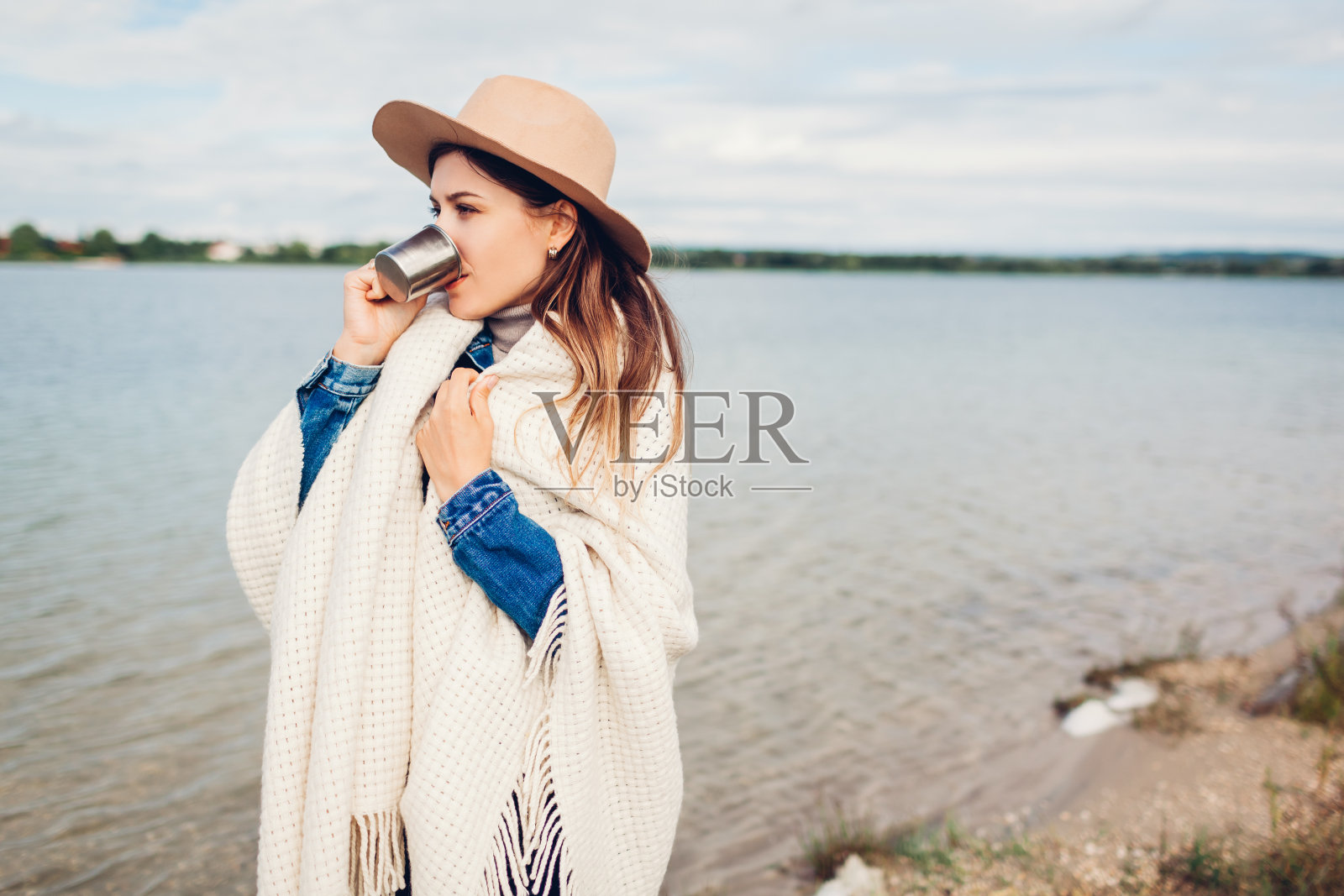 女游客戴着帽子，用毯子喝着热茶，欣赏湖景。旅游与旅游概念照片摄影图片