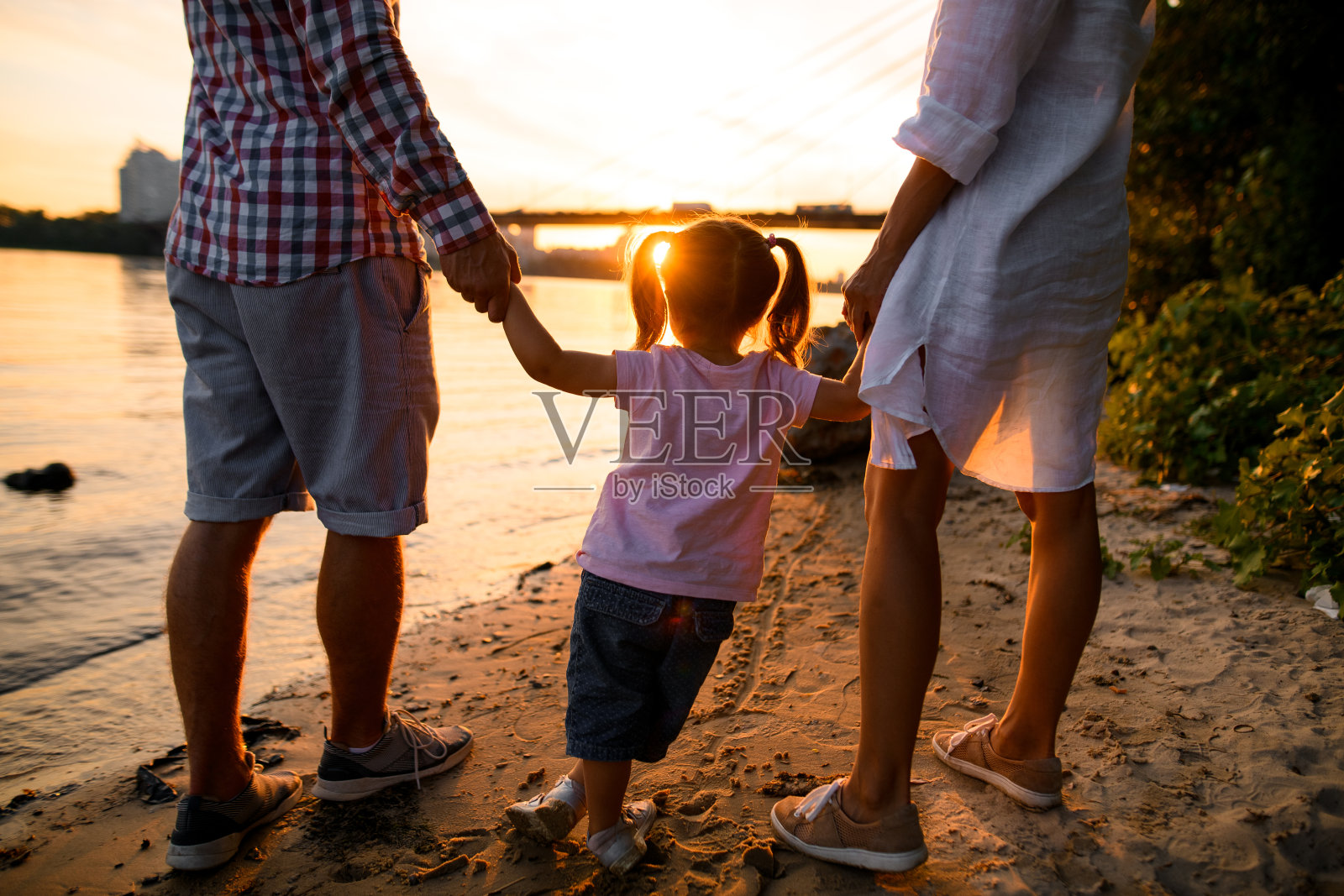 后视图年轻的家庭夫妇带着孩子沿着沙河岸散步照片摄影图片