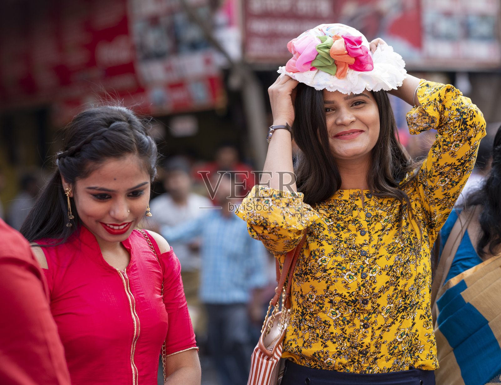 两个女孩在当地的街头市场买帽子。照片摄影图片
