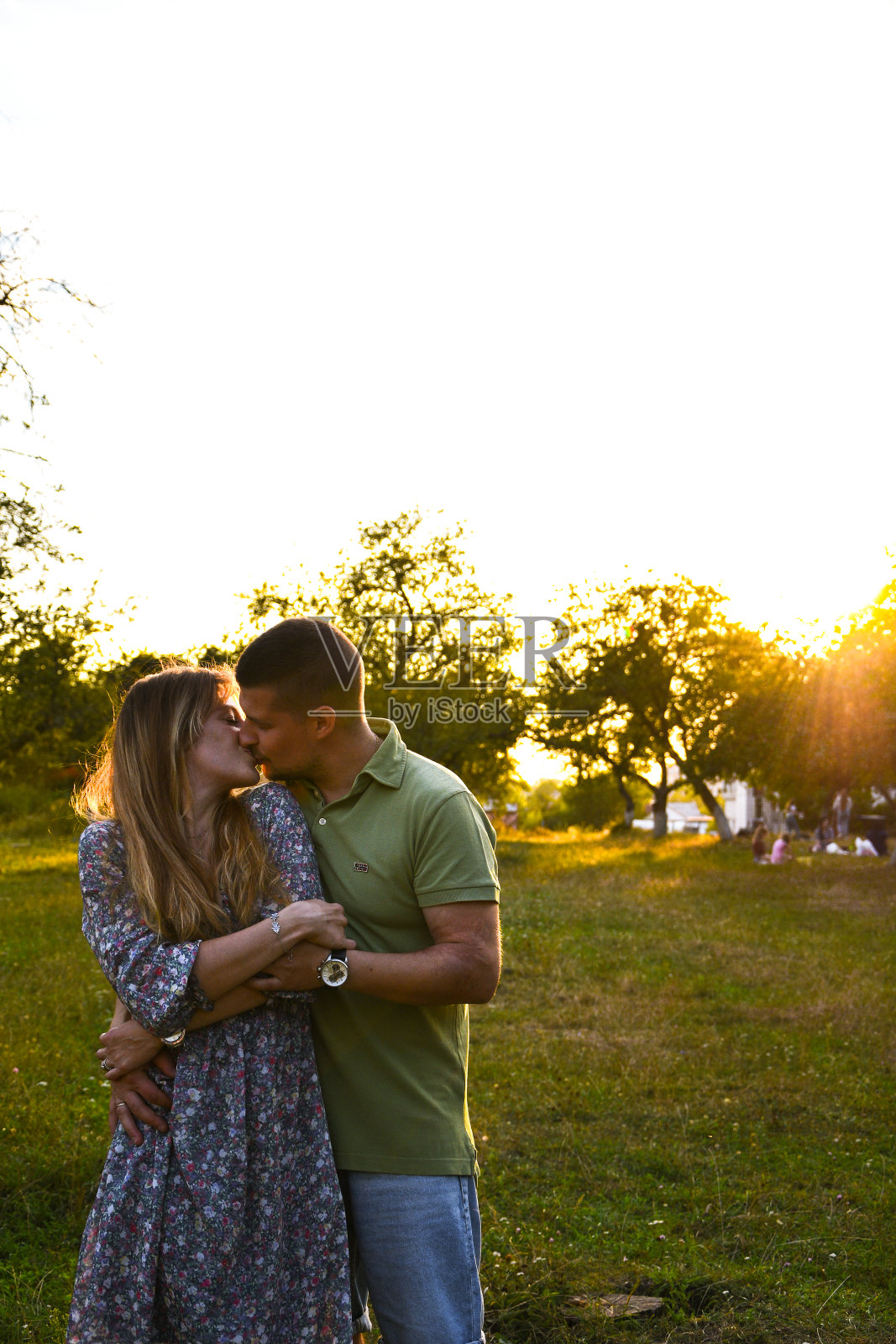 年轻的家庭妈妈爸爸在傍晚散步在一个公园与树木在夕阳的光。情侣接吻。幸福的年轻夫妇享受户外日落照片摄影图片