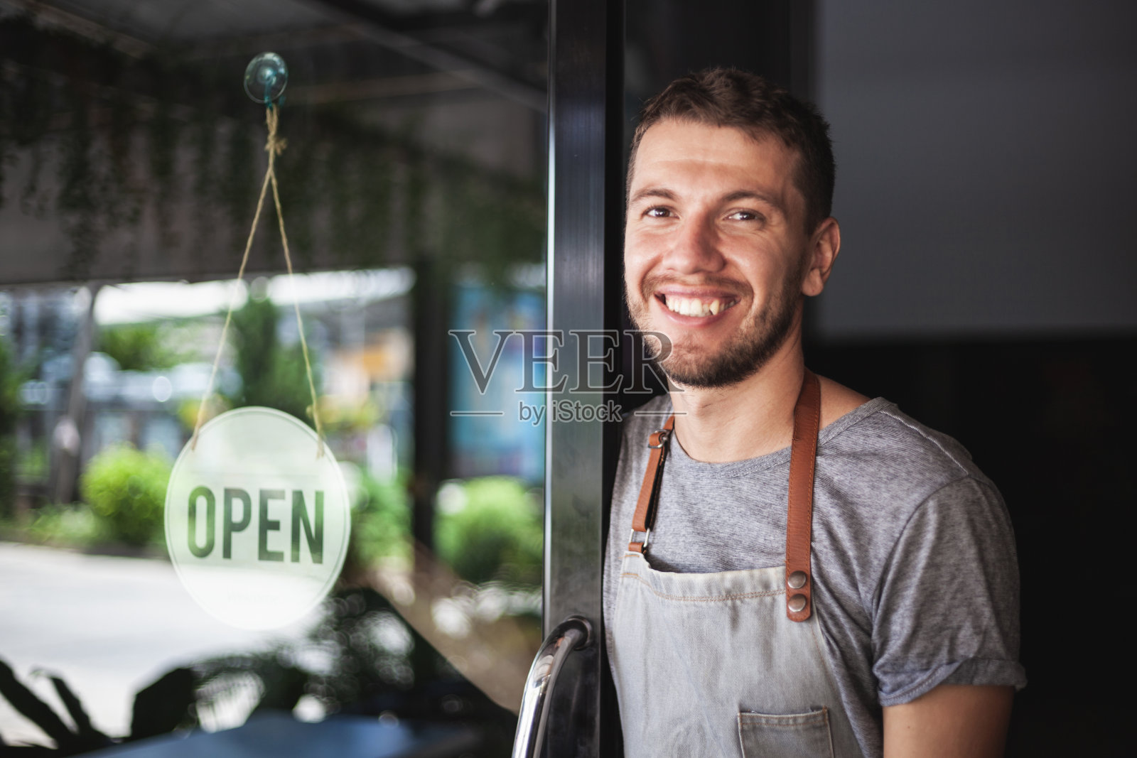 由于covid-19的隔离，寿司店的年轻厨师老板微笑着转向他的店重新开业的标志。小型企业在泰国帕岸市开张照片摄影图片