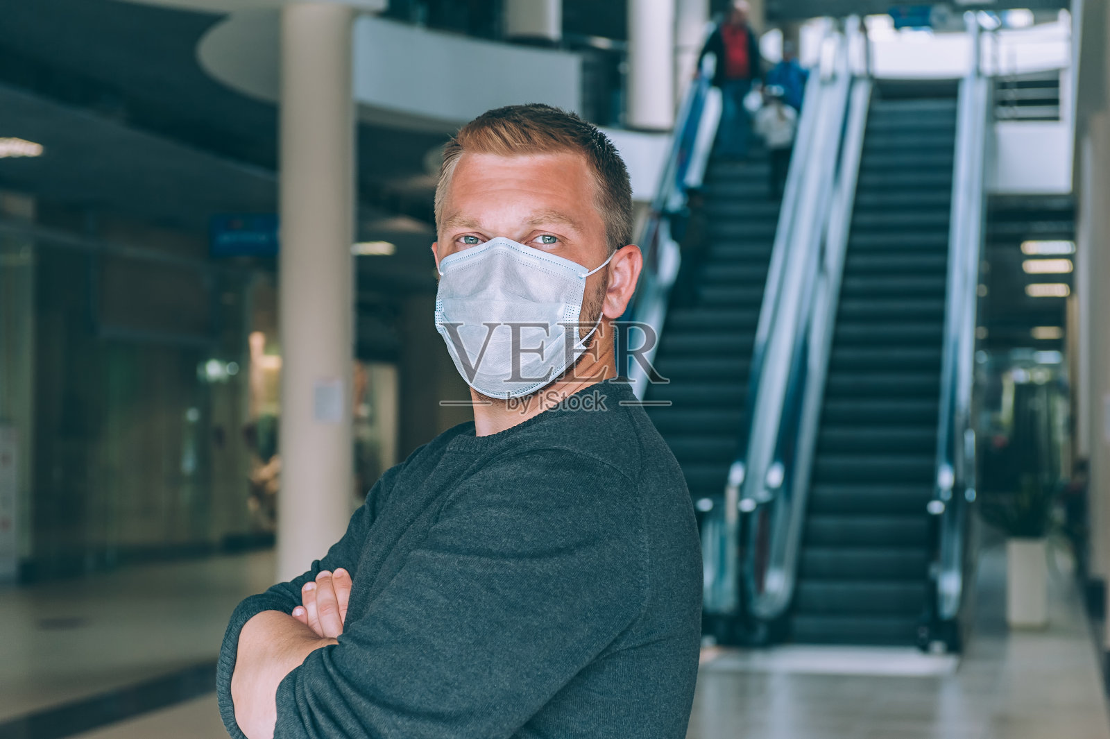 一个戴着医用面具的男人，背景是一个购物中心。COVID-19概念。照片摄影图片