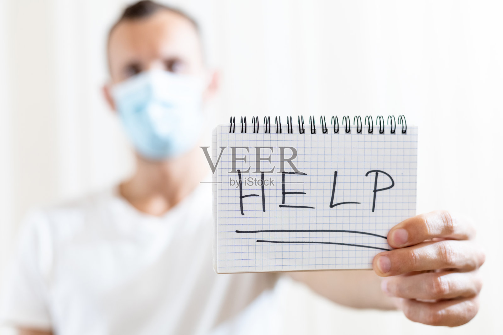 一名戴着医用口罩的男子展示了一张写有“帮助”字样的纸照片摄影图片