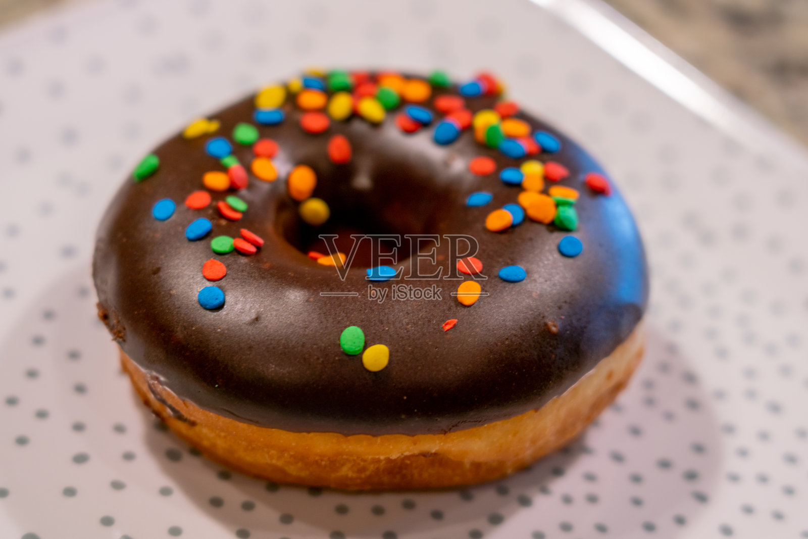 上面有彩色点缀的巧克力甜甜圈，白色的盘子上有灰色的点照片摄影图片