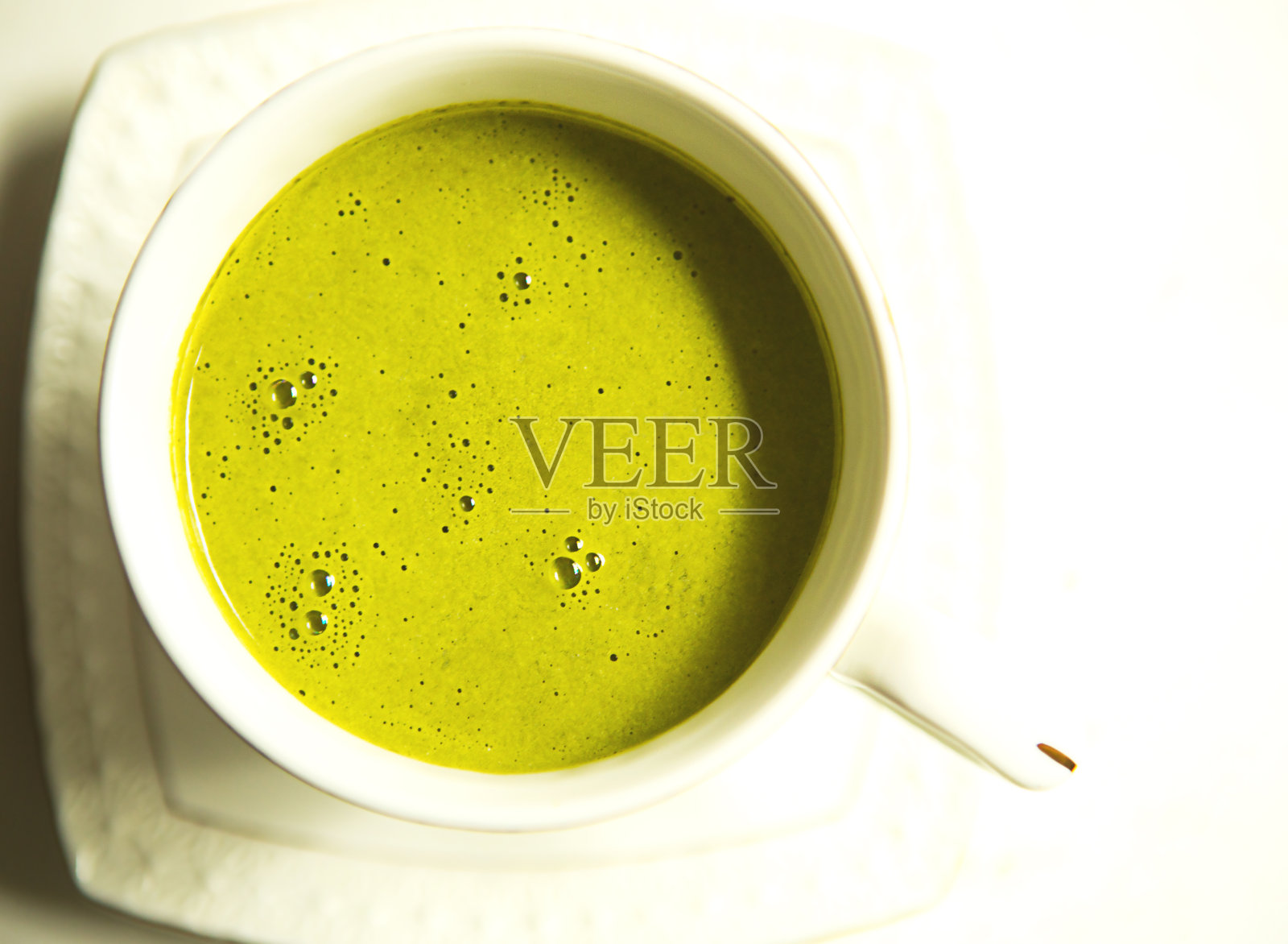 日本抹茶绿茶倒入一个白色的马克杯和一个白色的茶碟粉末。茶具放在有花纹的餐巾上。照片摄影图片