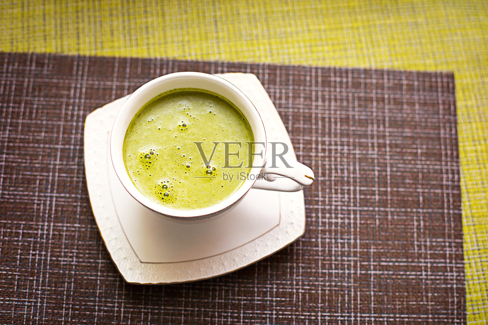 日本抹茶绿茶倒入一个白色的马克杯和一个白色的茶碟粉末。茶具放在有花纹的餐巾上。照片摄影图片