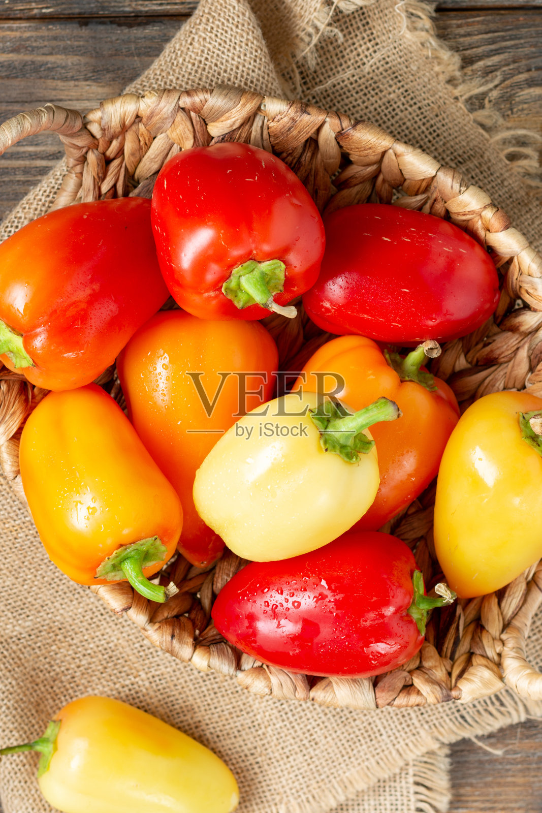 甜辣椒。红色、黄色和橙色的辣椒放在一个篮子里，放在棕色的木桌上。辣椒特写照片摄影图片