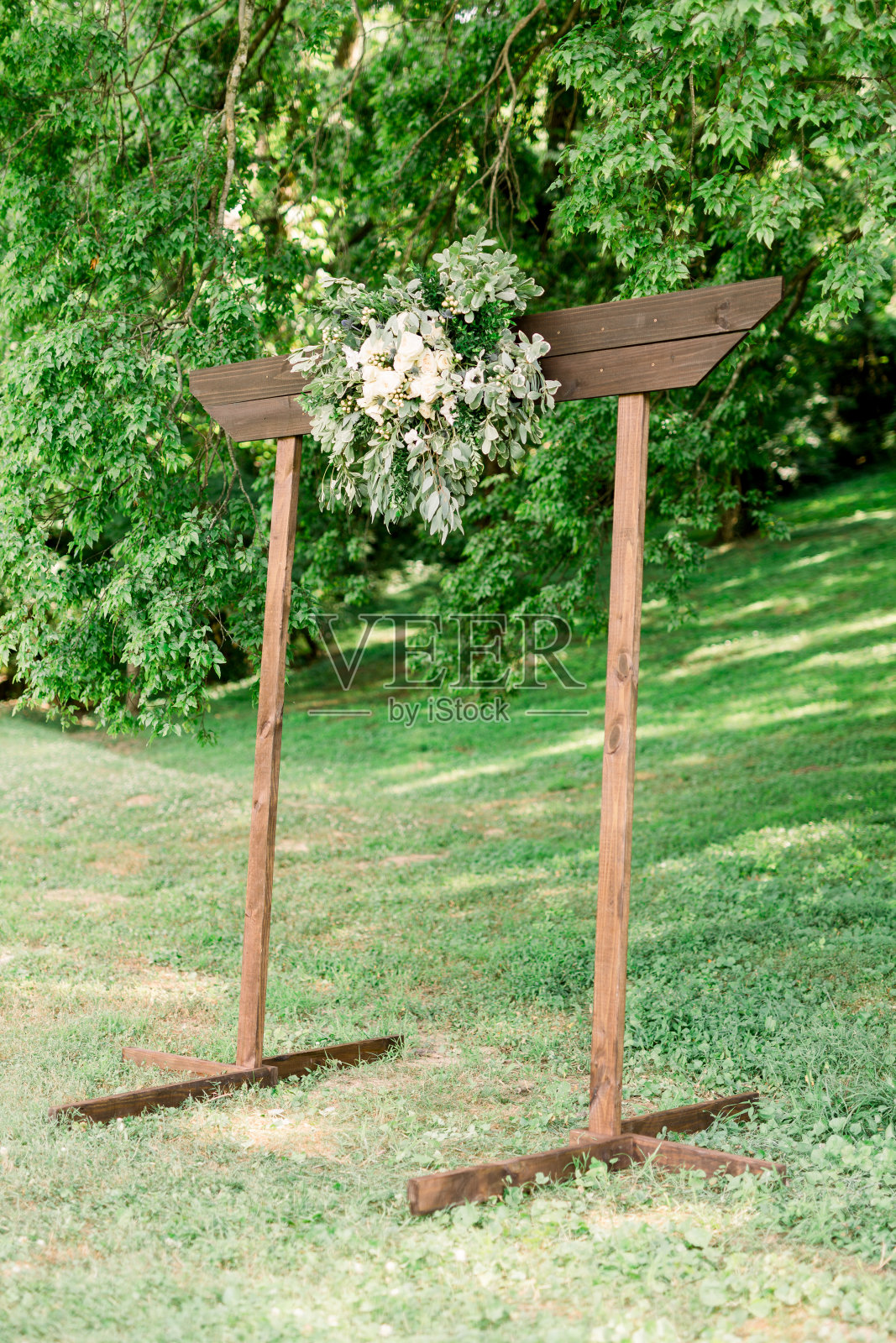 简单的婚礼拱门，由白色玫瑰和绿叶组成，设置在一个以灌木丛为背景的公园里。照片摄影图片