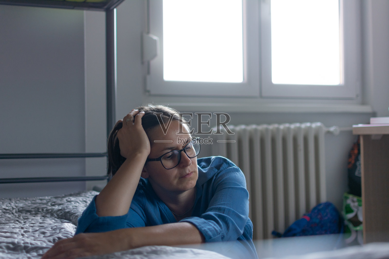 焦虑的中年妇女坐在地板上，靠着床，感到担忧照片摄影图片