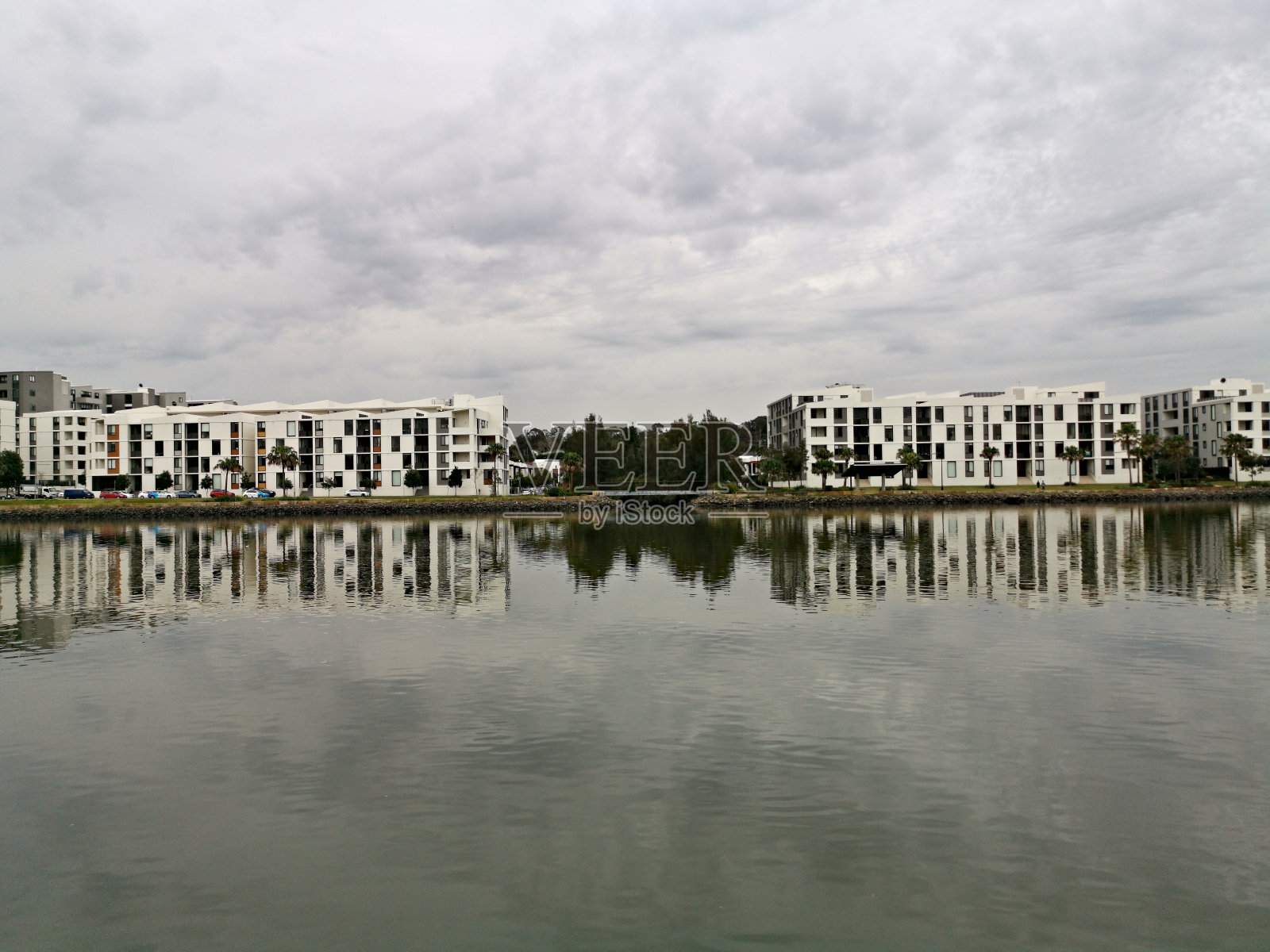 美丽的河流景观与现代公寓楼，多云的天空和树上的倒影照片摄影图片