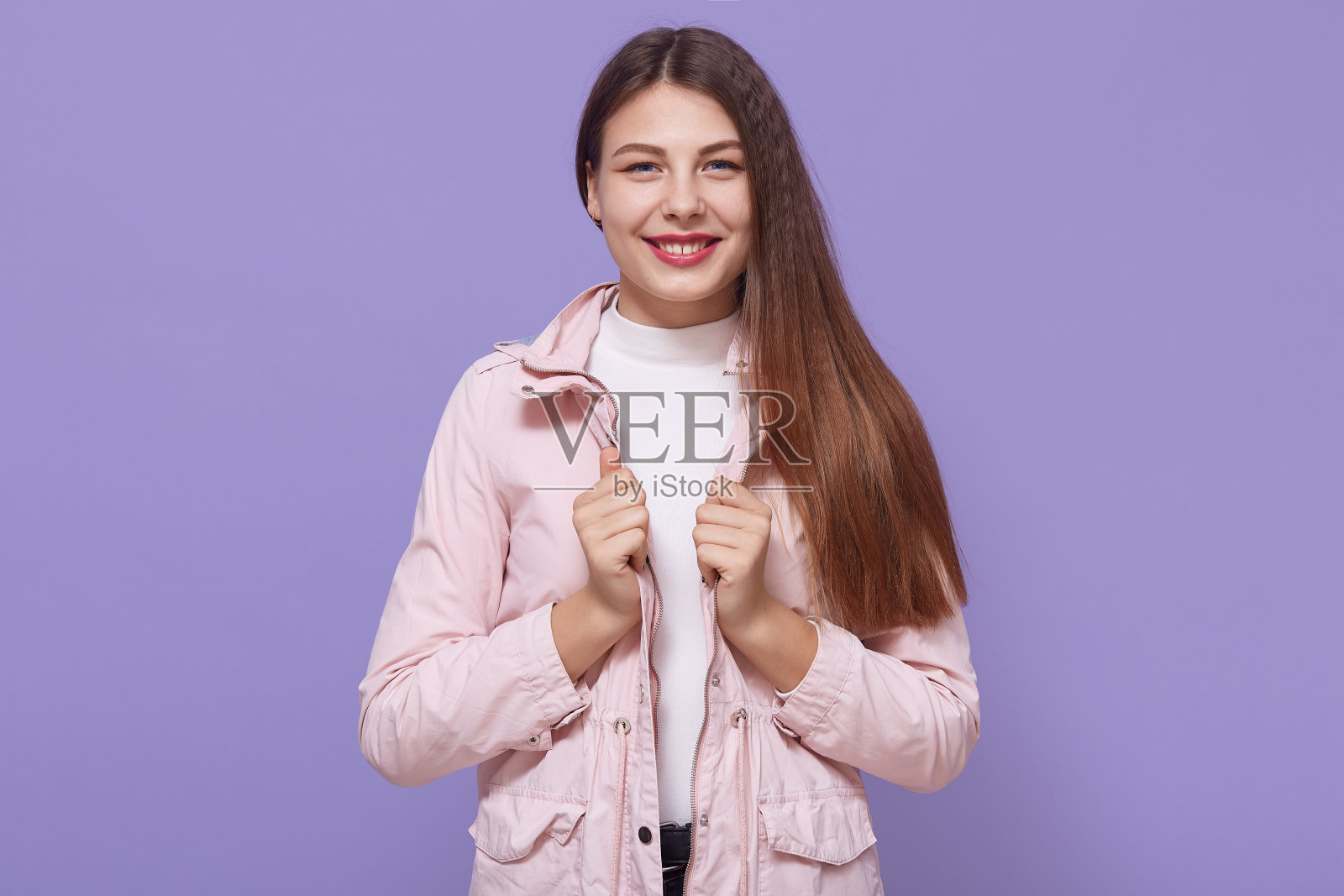 肖像微笑的女性迷人的微笑，迷人的美丽的女孩穿着淡粉色夹克，看着相机，摆出孤立的丁香背景。照片摄影图片
