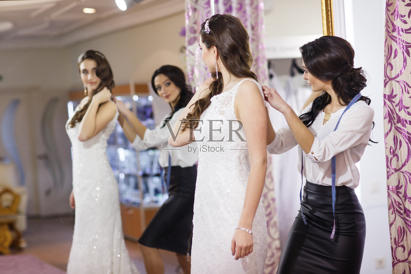一位女士在一家商店试穿婚纱，旁边有一位女店员。照片摄影图片