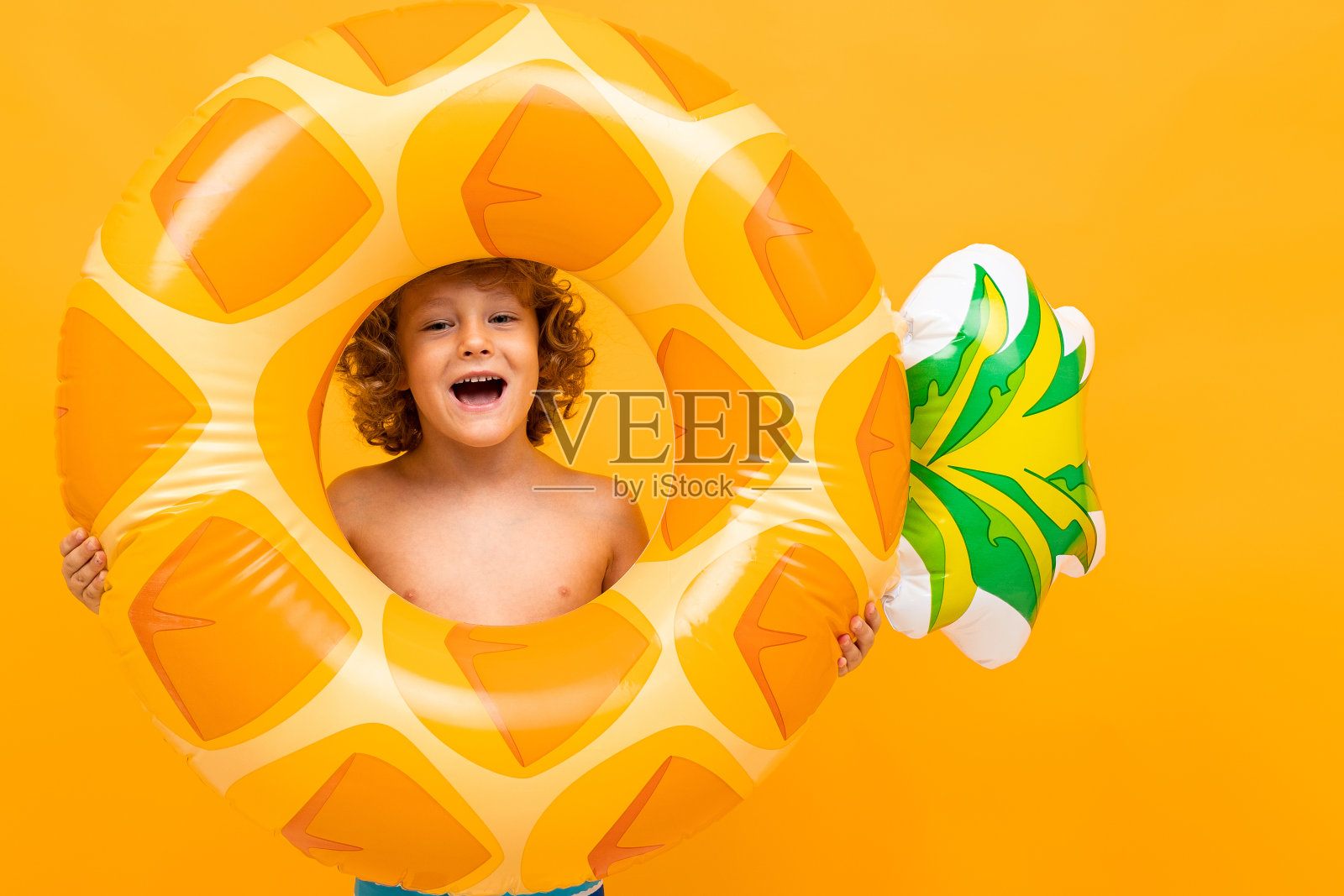 小男孩的卷发在泳衣和大橡胶圈孤立在黄色的背景照片摄影图片
