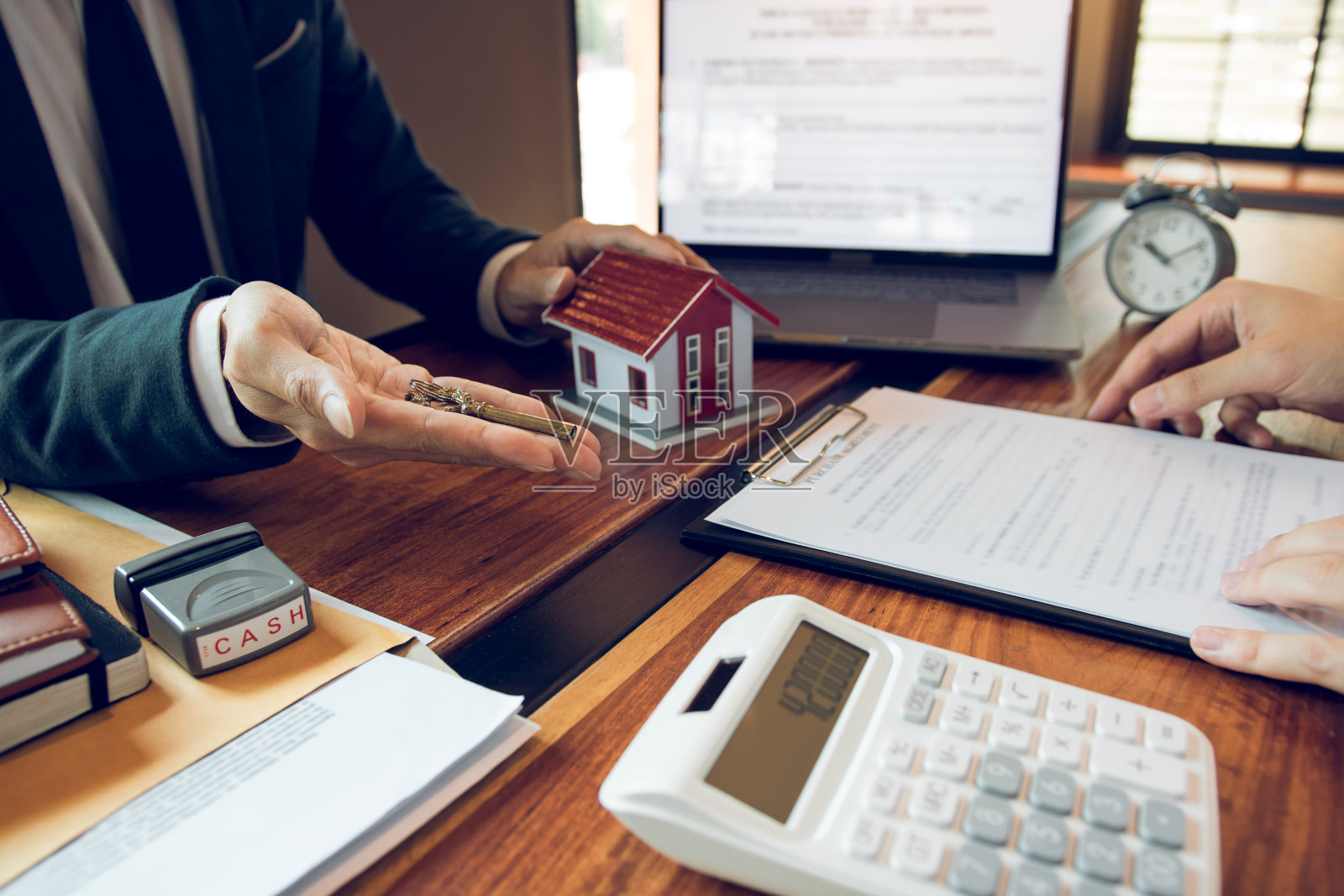 房地产经纪人的手传递钥匙的新业主在办公室与买方房子的概念。照片摄影图片