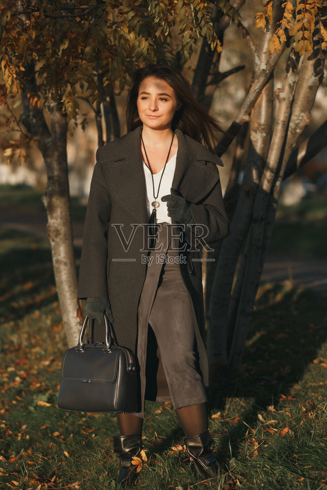 时尚的白人女孩在美丽的阳光明媚的秋天胡同皮草大衣手提箱照片摄影图片