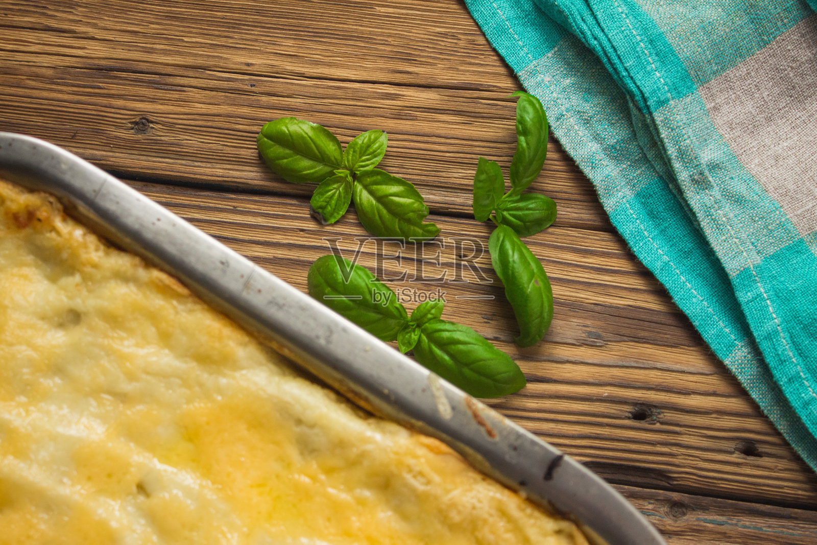 自制的烤宽面条放在金属烤盘里，配上罗勒叶、番茄、大蒜、盐、黑胡椒和绿松石桌布，放在棕色的木头背景上。前视图。照片摄影图片