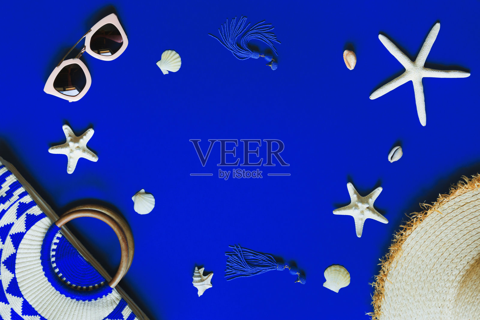 女士沙滩配饰:包、草帽、太阳镜、耳环、海星、贝壳等电光蓝底色。照片摄影图片