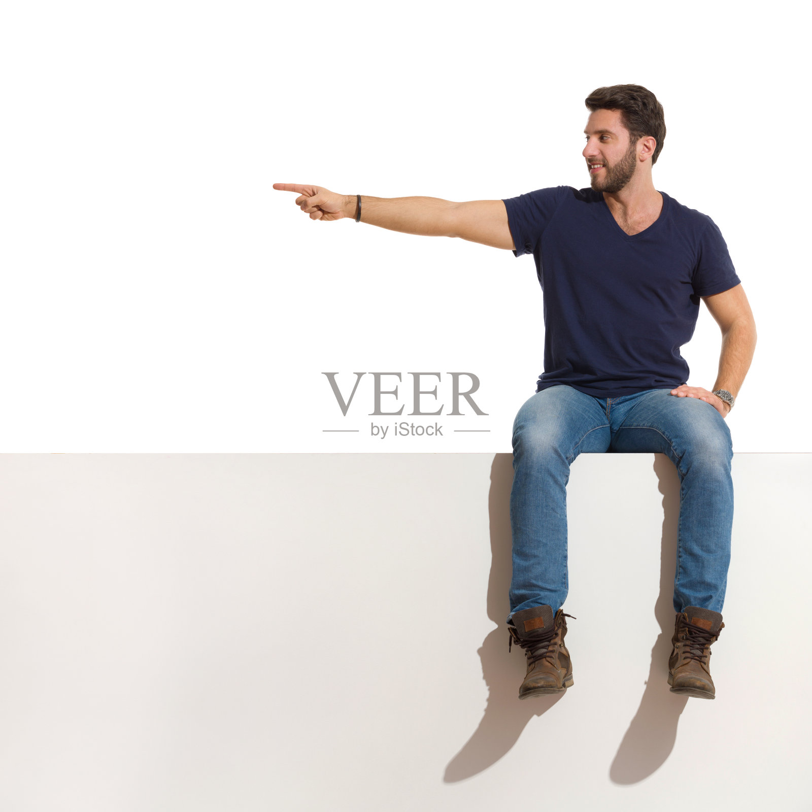 快乐英俊的男人坐在上面指着一边看照片摄影图片