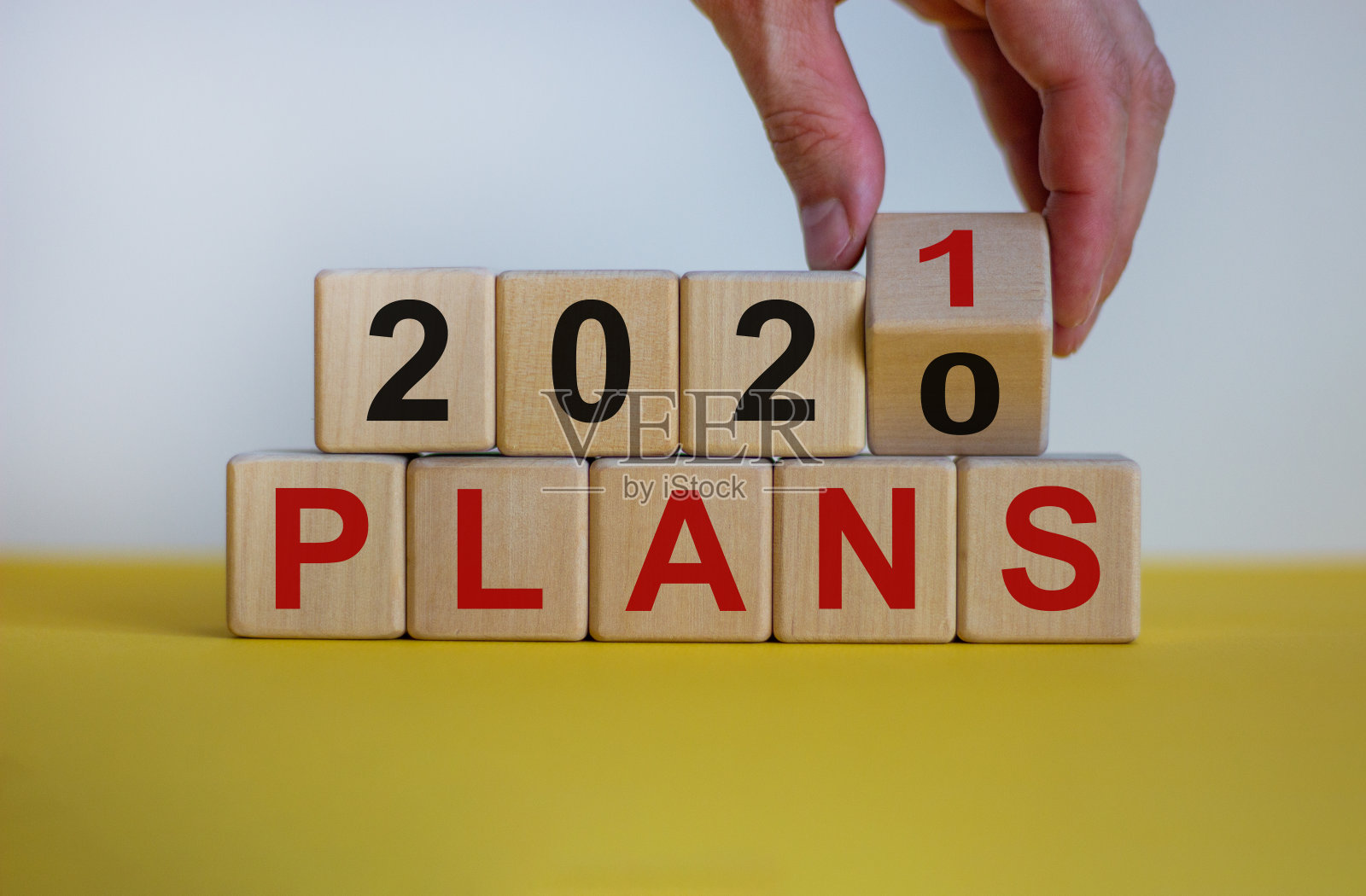规划2021年的经营理念。男性手翻木方，将“2020计划”改成“2021计划”。漂亮的黄色表，白色背景，拷贝空间。照片摄影图片